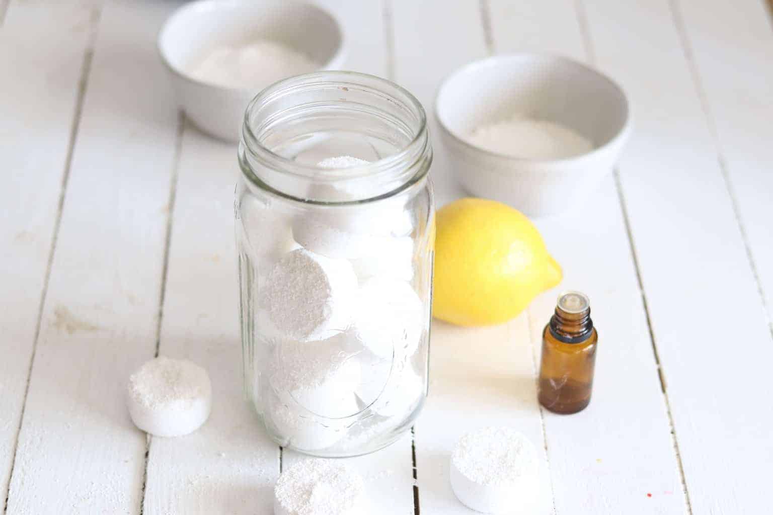 Homemade dishwasher soap pods in mason jar with ingredients on wooden table.