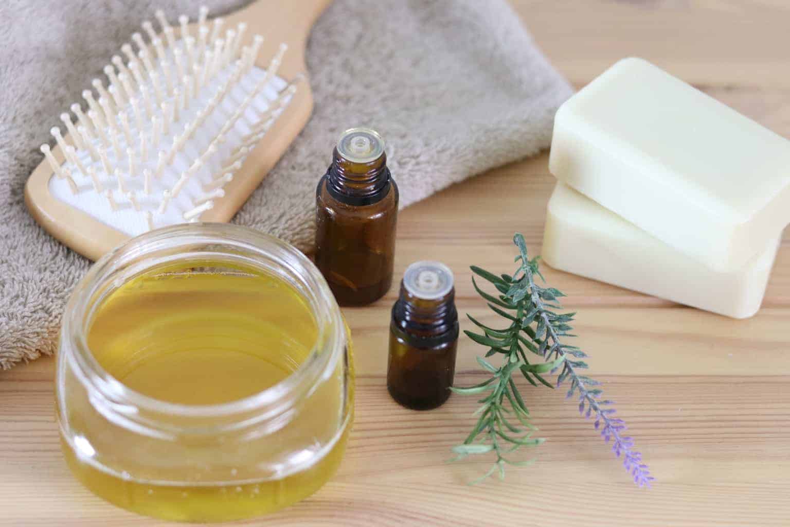 Healthy homemade conditioner on table with hair brush, soap bars, and essential oil bottles.