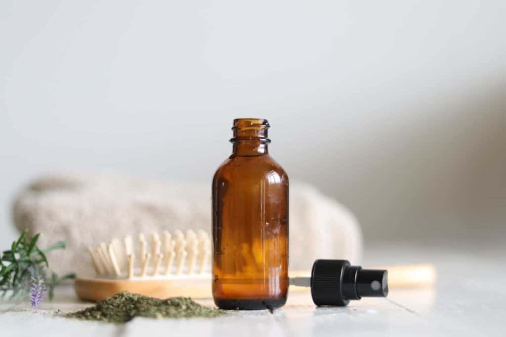 DIY hair serum on a white bathroom vanity with a small pile of dried nettle and a hair brush.
