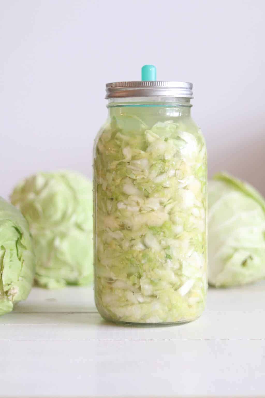 Sauerkraut in mason jar with fresh cabbages on white table.