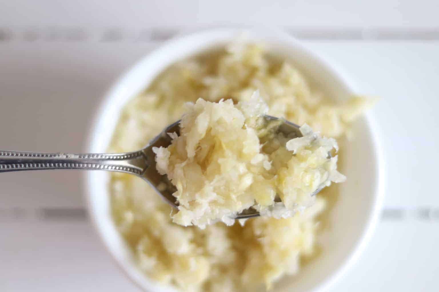 Spoon full of sauerkraut with bowl of sauerkraut in background.