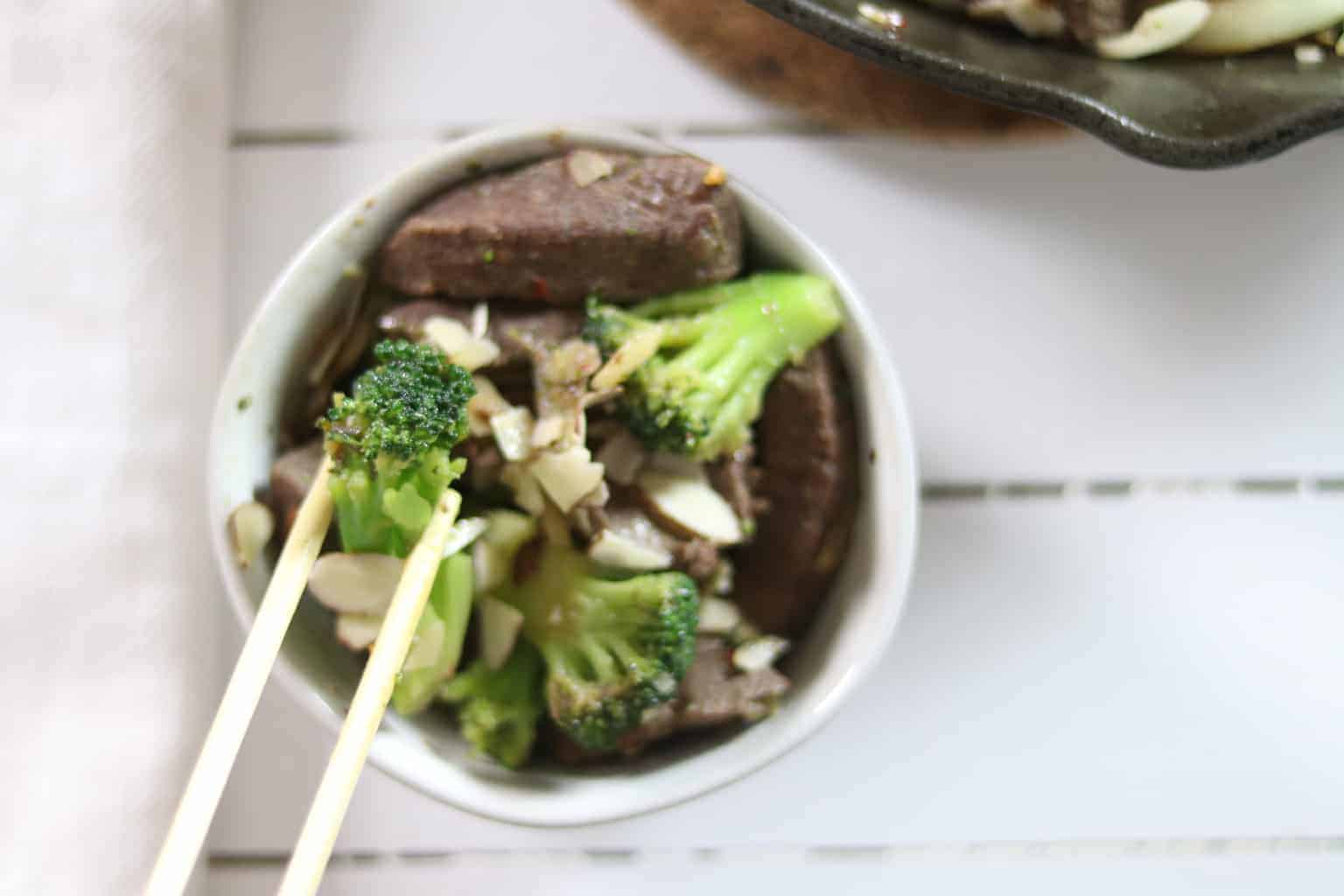 Beef chunks and broccoli in white bowl topped with chopped almonds. 