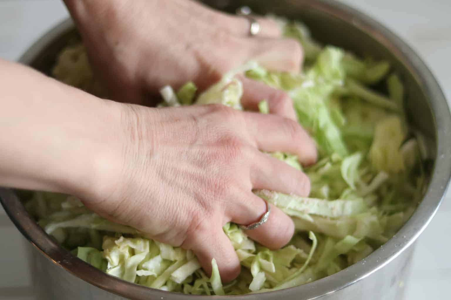 Hands mixing cabbage to make brine.