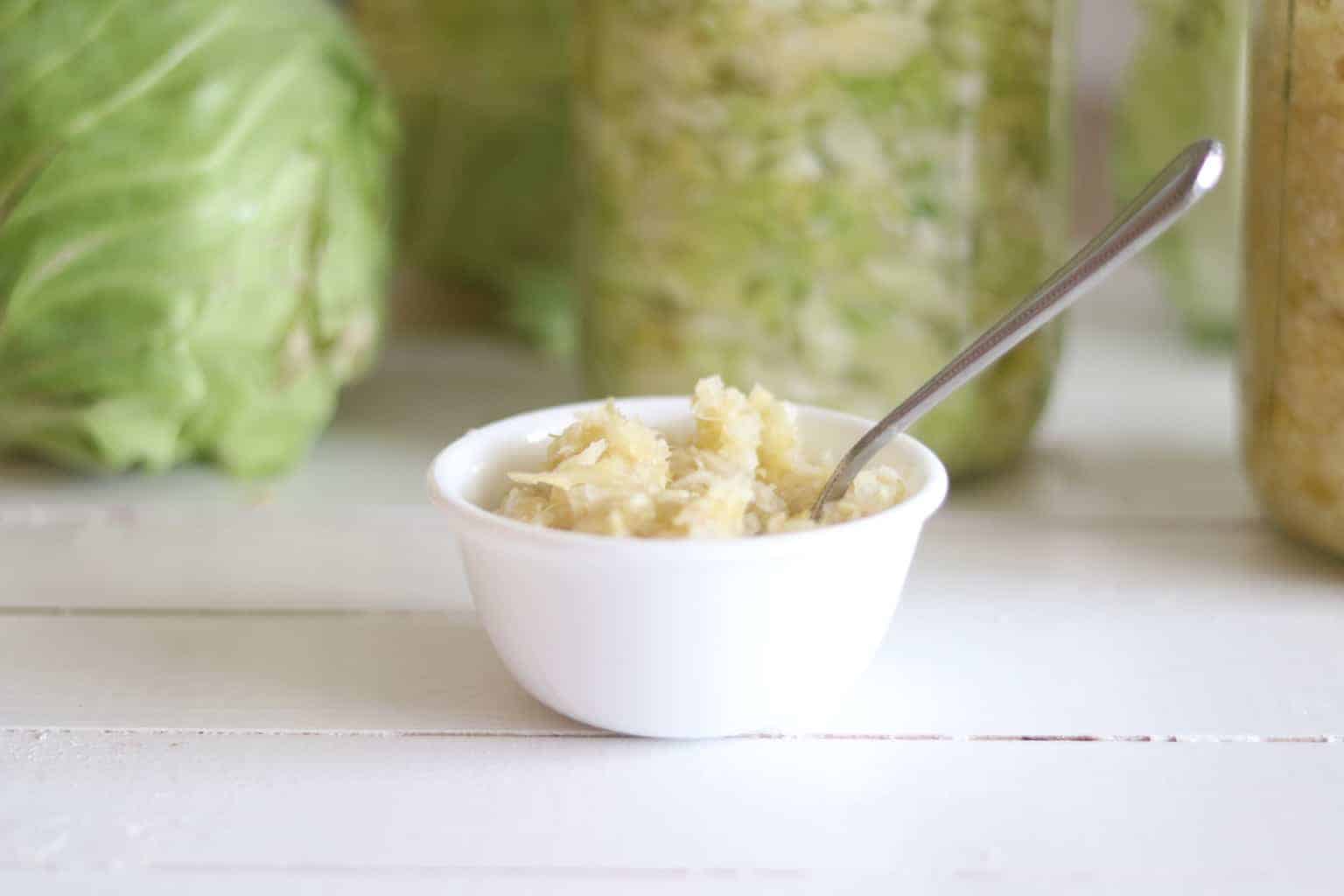 Small white bowl of sauerkraut with cabbage in background.