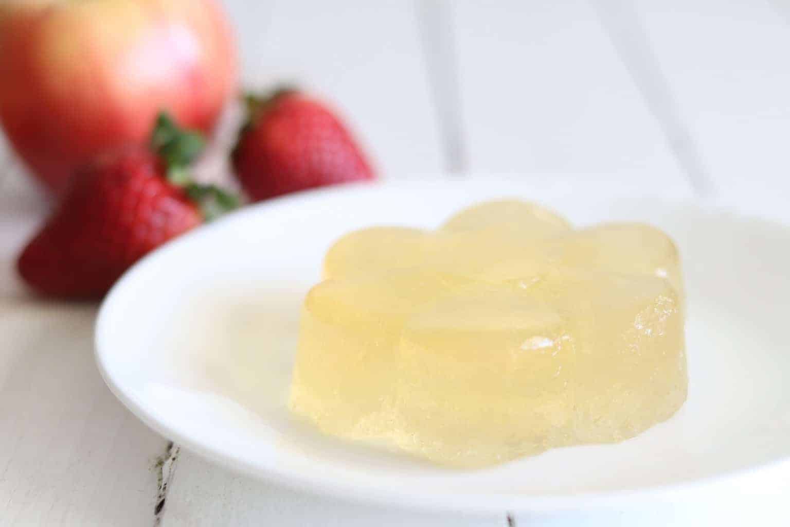 Flower shaped jello on plate and in white background fresh strawberries and an apple.