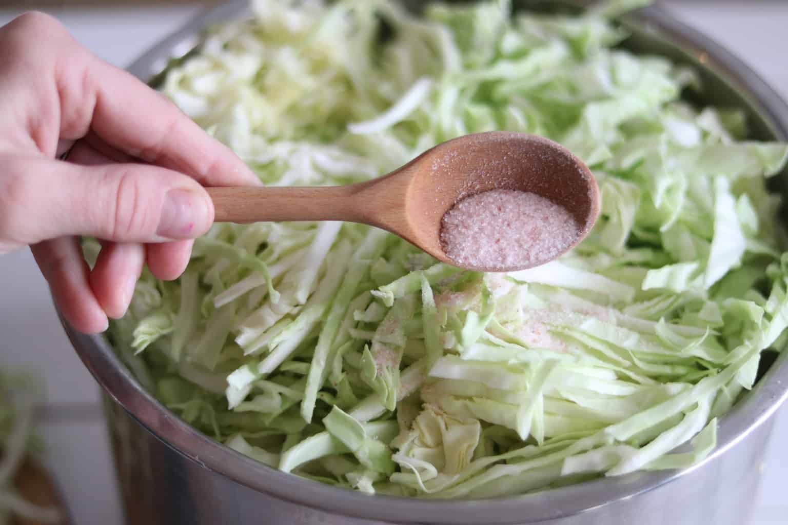 Shredded cabbage with pink Himalayan salt in large bowl.