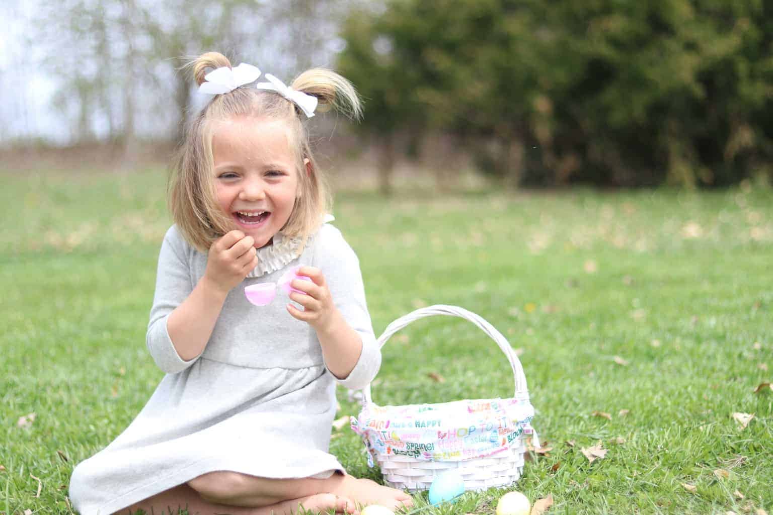 Little girl sitting on grass with an Easter basket by her.