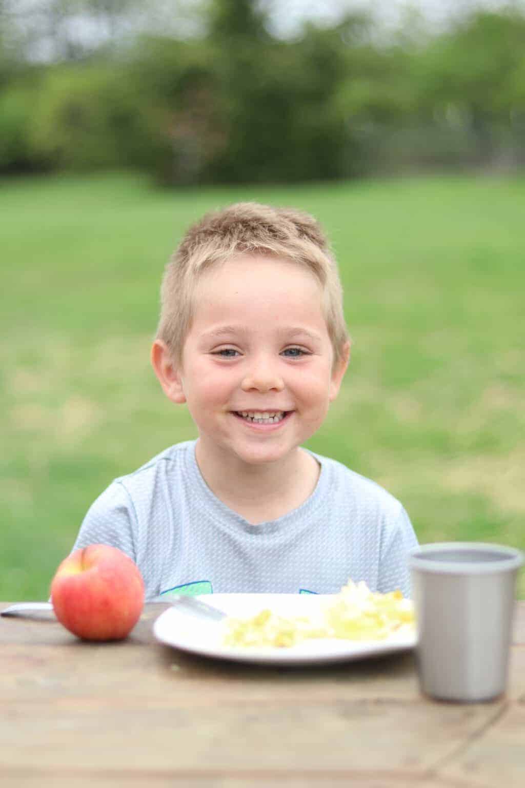A little boy eating a healthy meal outside.