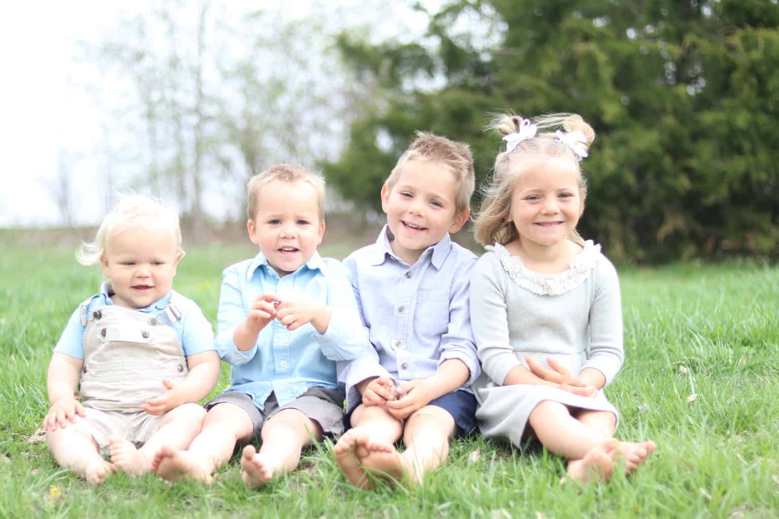 Four little children sitting on the grass.