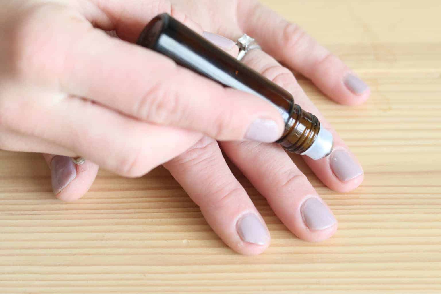 Women rolling essential oil roller bottle on finger nails.