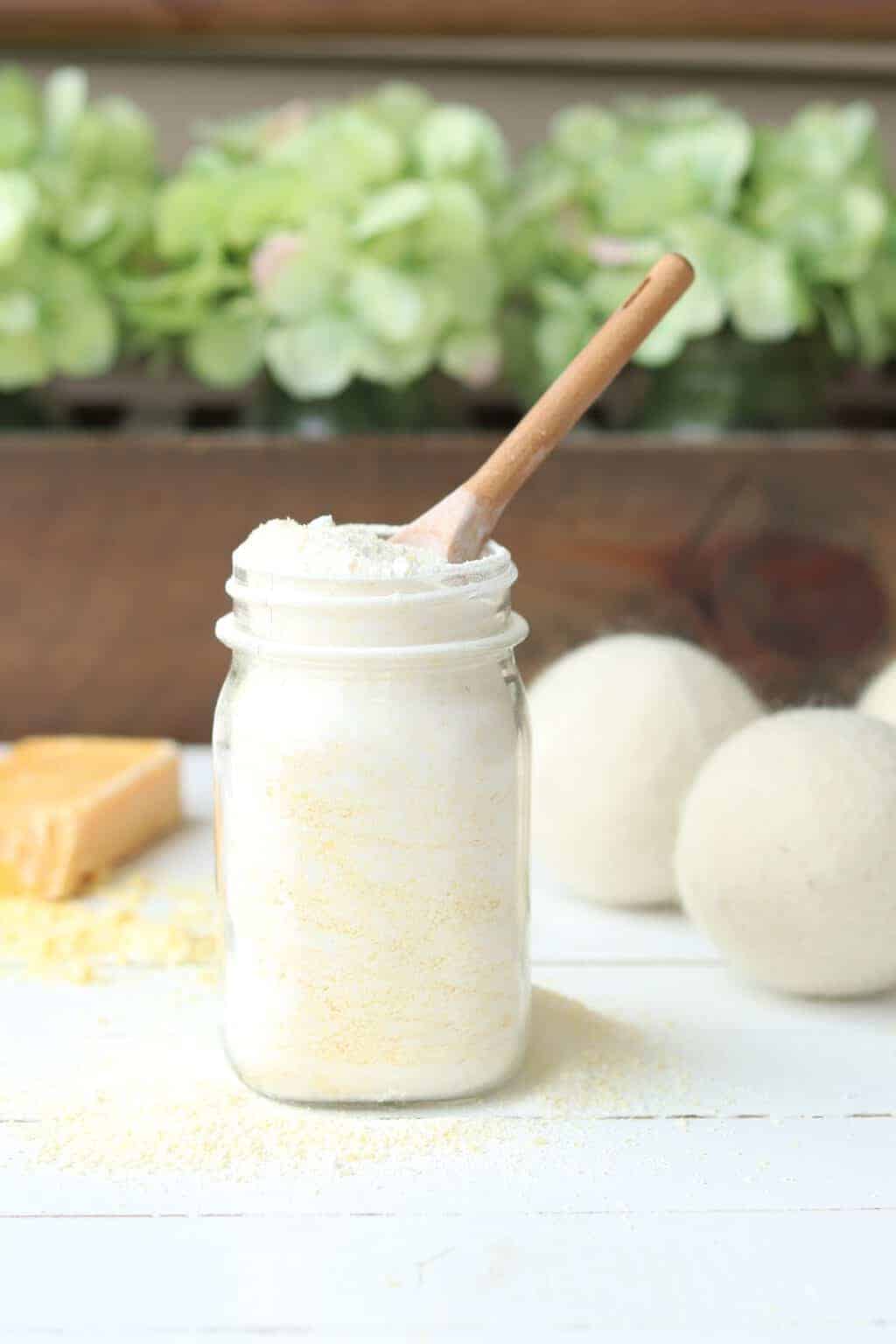 Powder laundry soap in mason jar on table with flowers, soap bar and dryer balls.