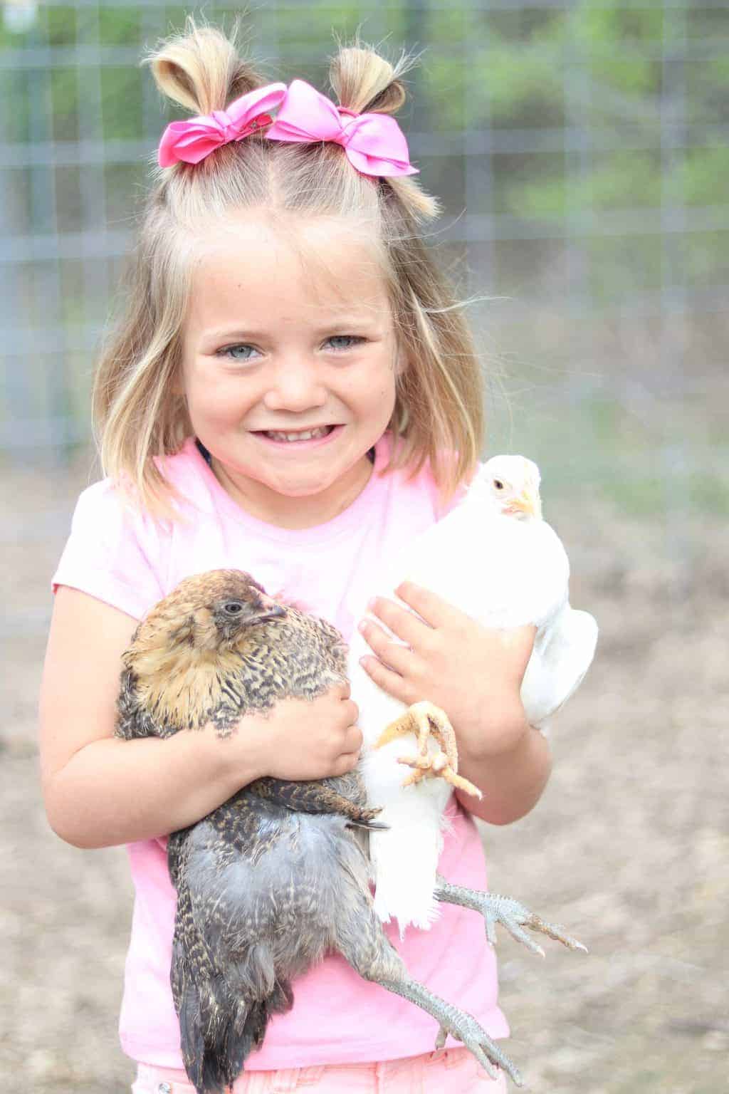 A little girl holding chickens outside.