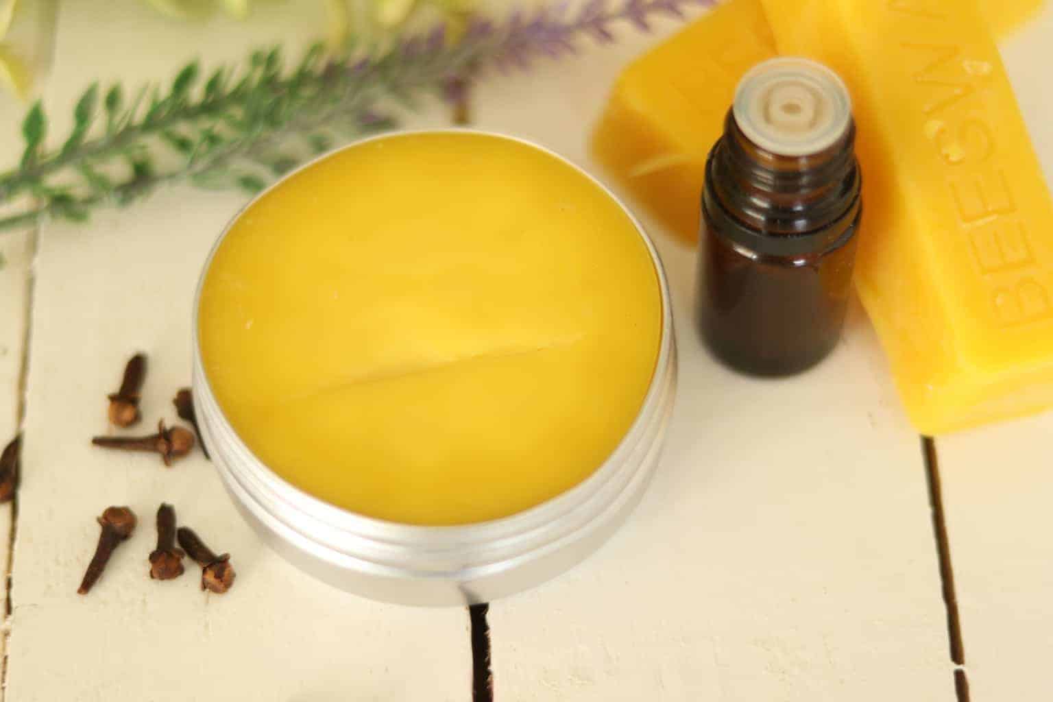 Solid perfume on wooden table with essential oil bottle, beeswax, and flowers.