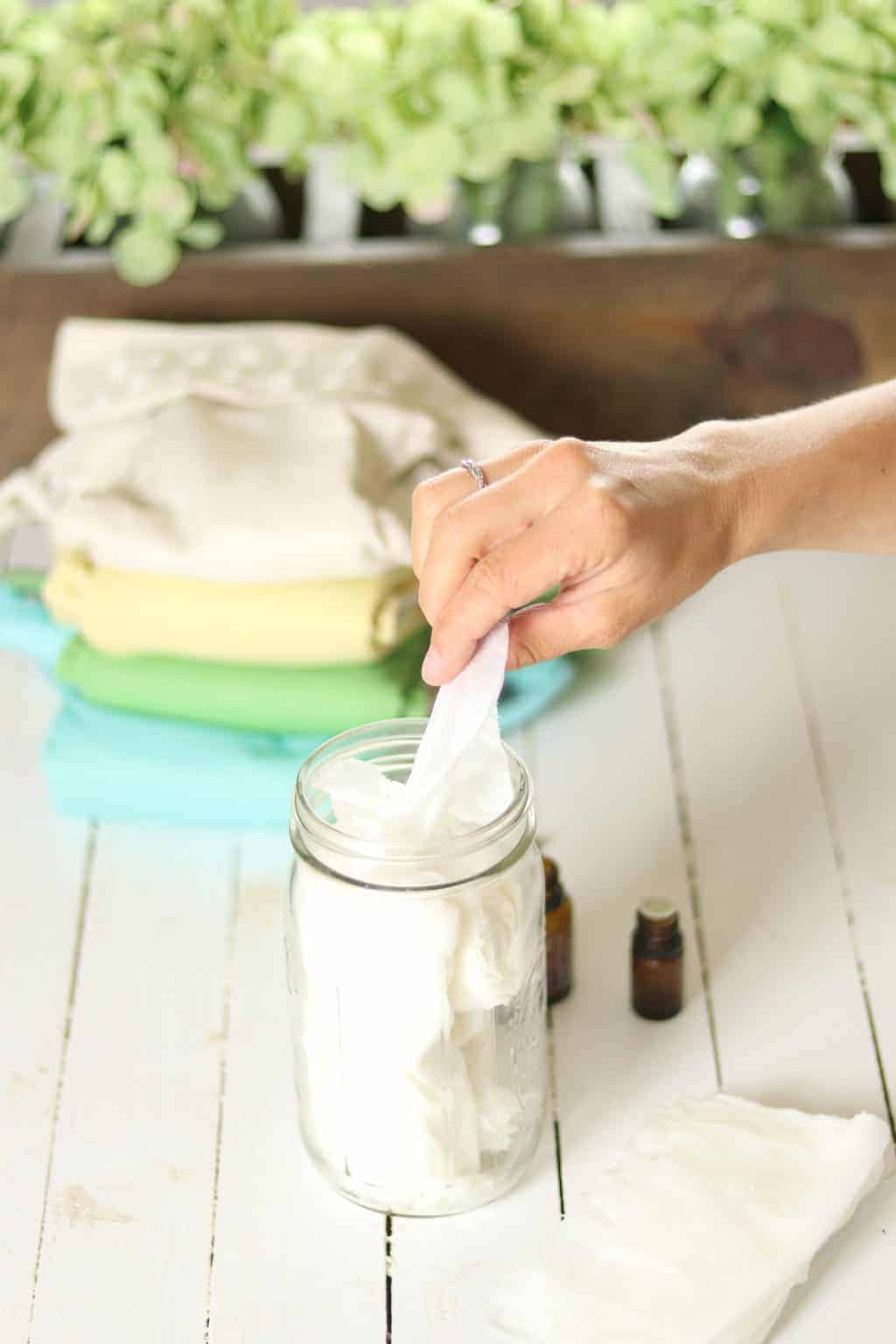 Baby wipes in mason jar with flowers and cloth diapers on wooden table.