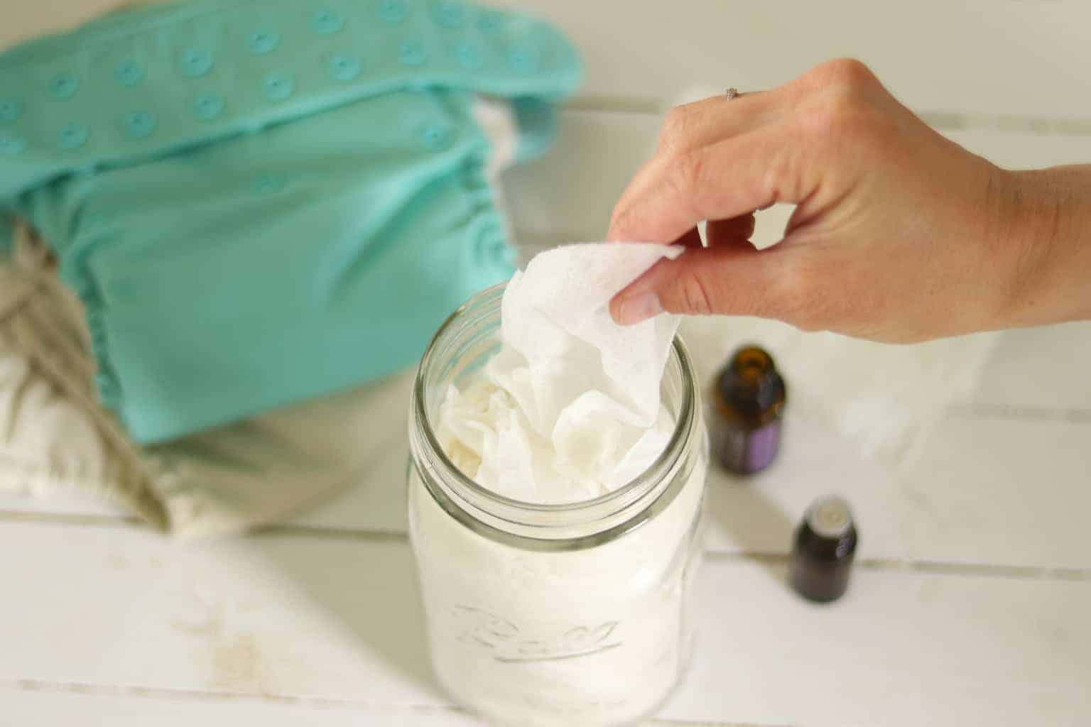 Homemade baby wipes in mason jar with cloth diapers on table.