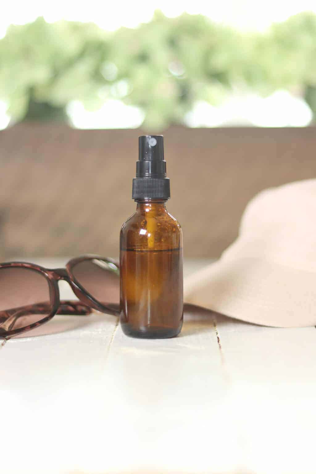 Sunburn relief spray in 2 ounce amber glass bottle with sun glasses and ballcap on table.