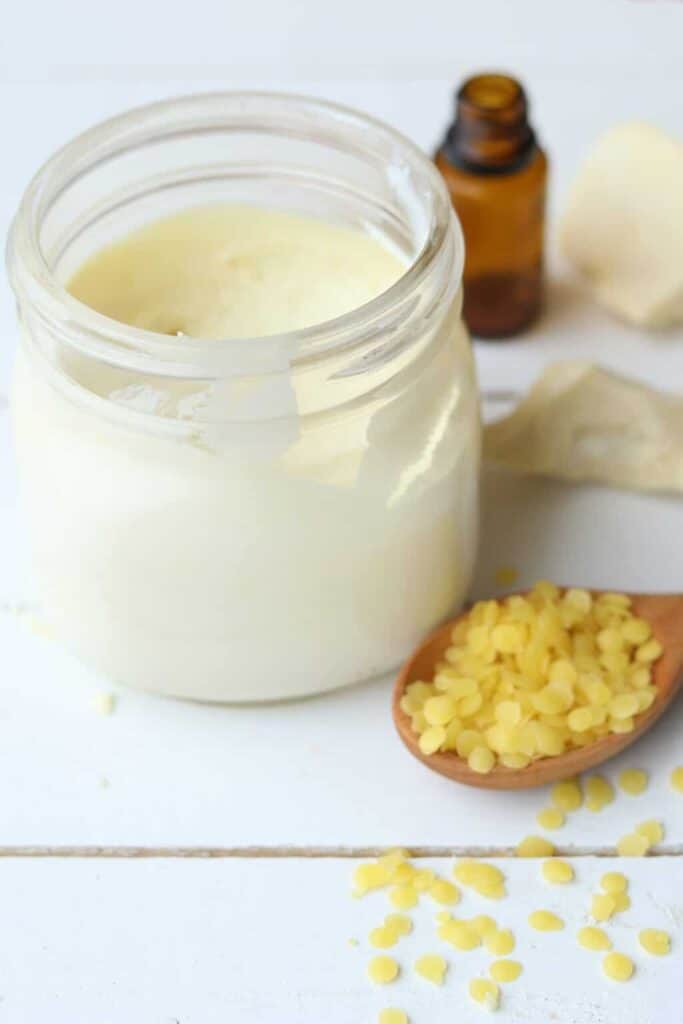 Diy sunscreen in glass container on wooden shiplap table with a wooden spoon of beeswax pellets.