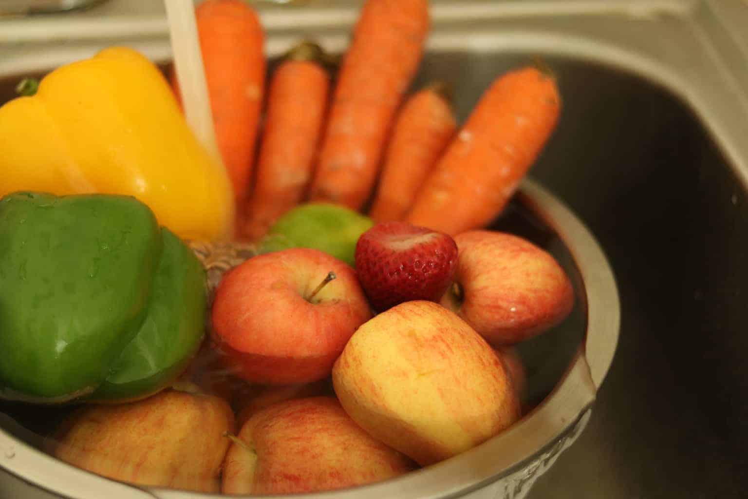 Fruit and vegetables in sink under running water.
