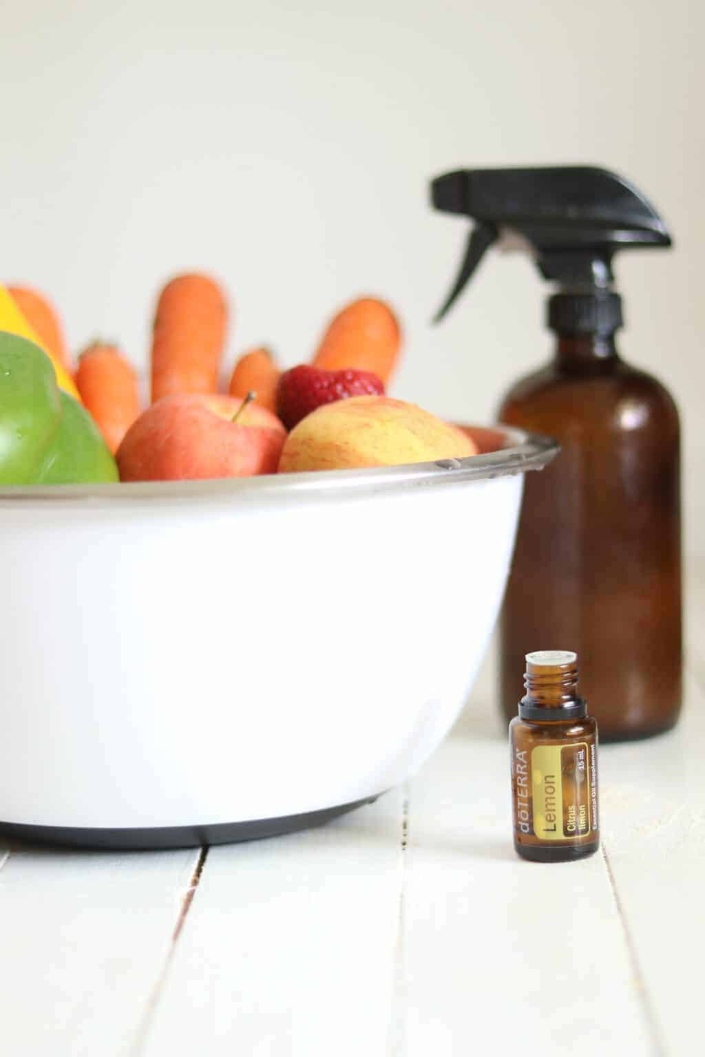 Fruit in a white bowl with spray bottle and essential oil bottle.