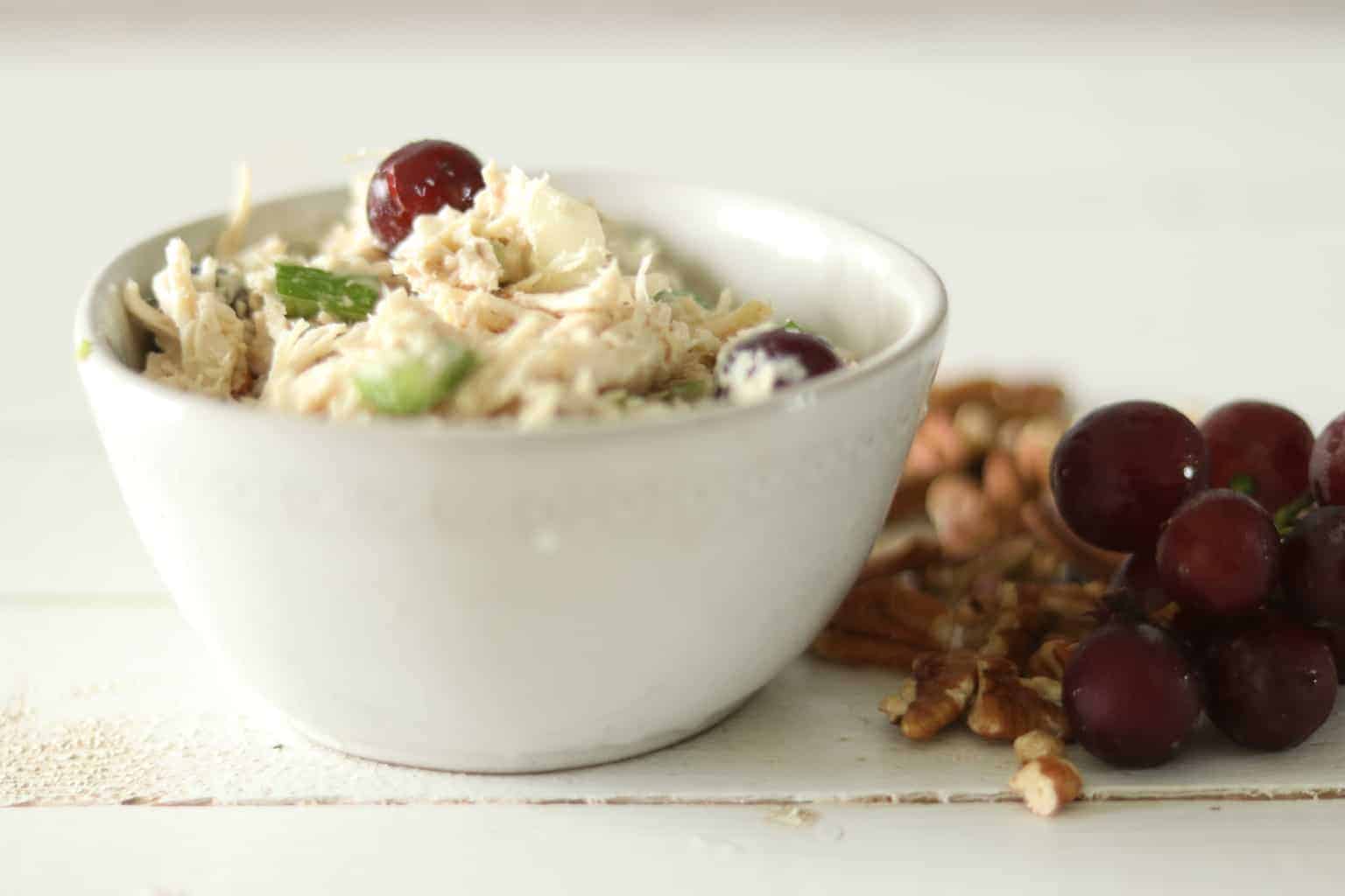 Healthy chicken salad in glass bowl with pecans and grapes on table.