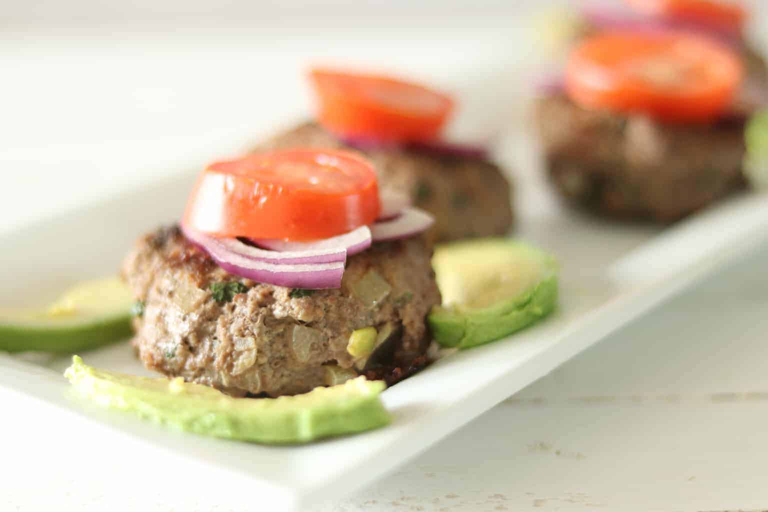 Homemade burgers with tomatoes, red onion, and avocado.