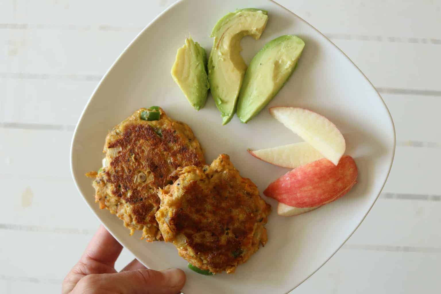 Salmon burgers with sliced avocado and apples.