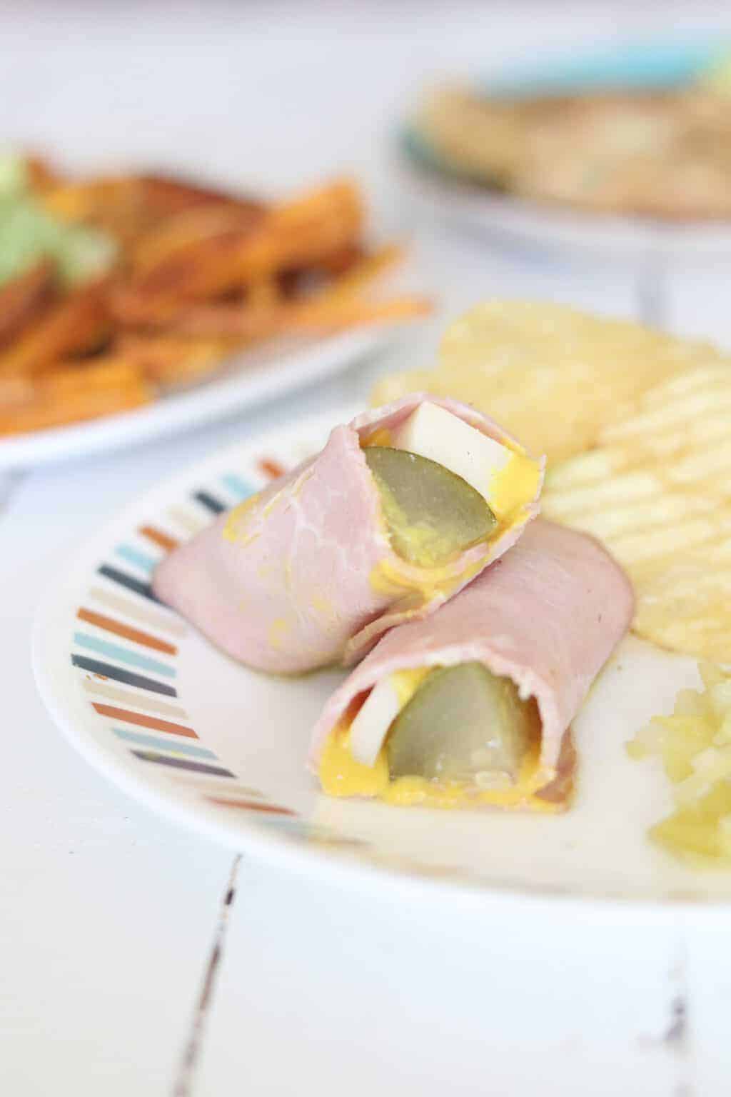Ham roll up with chips on plate sitting on wooden table.