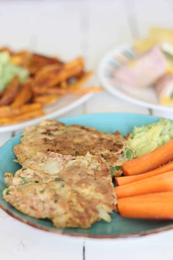 Salmon burgers, guacamole, carrot slices, sweet potato fries on plates.