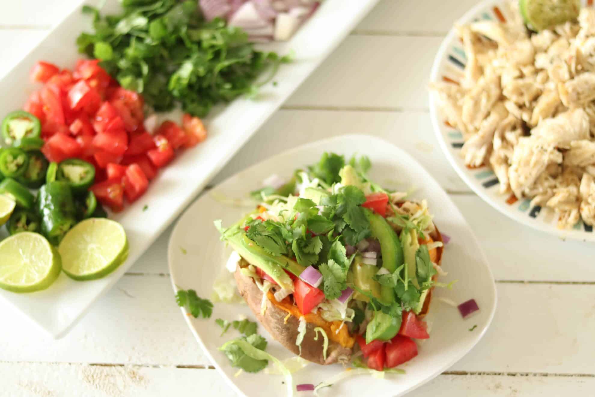 Chopped cilantro, tomatoes, chicken, and a Mexican stuffed sweet potato on white ship lap.