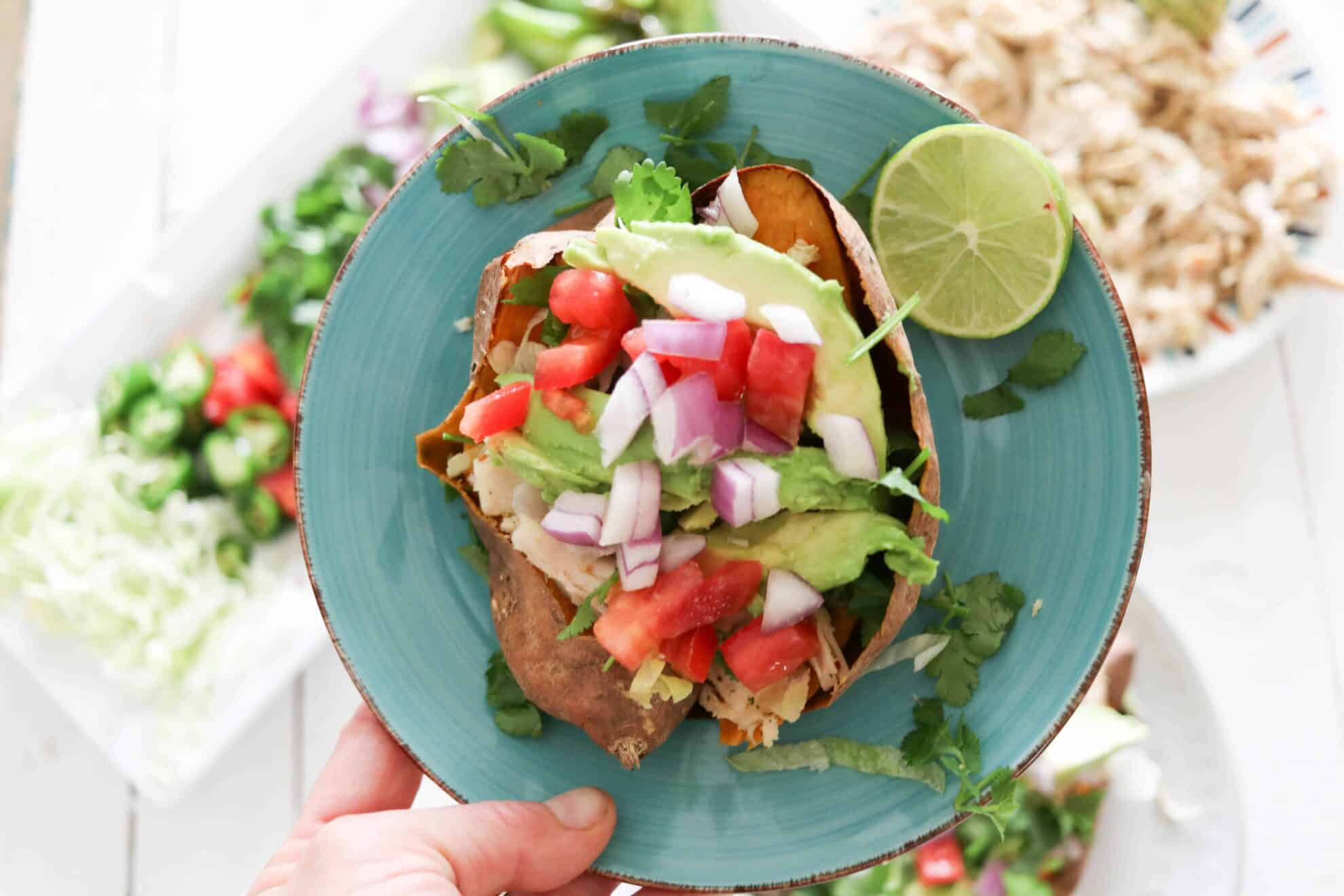 Mexican style stuffed sweet potato on blue plate with toppings in background.