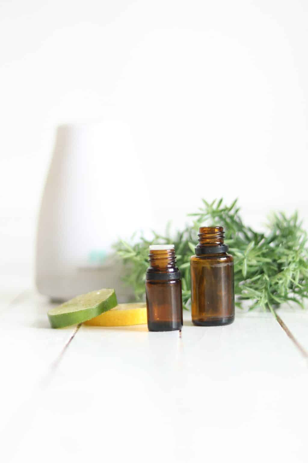 Essential oil diffuser on table with oil bottles, citrus fruit, and pine needles.