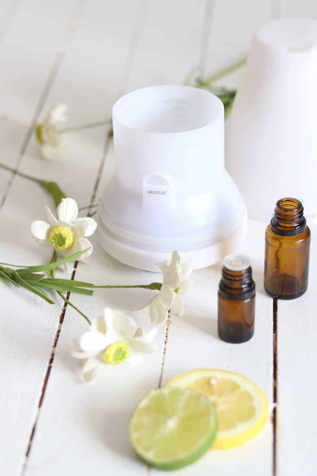 Essential oil diffuser with amber oil bottles and flowers on white shiplap.