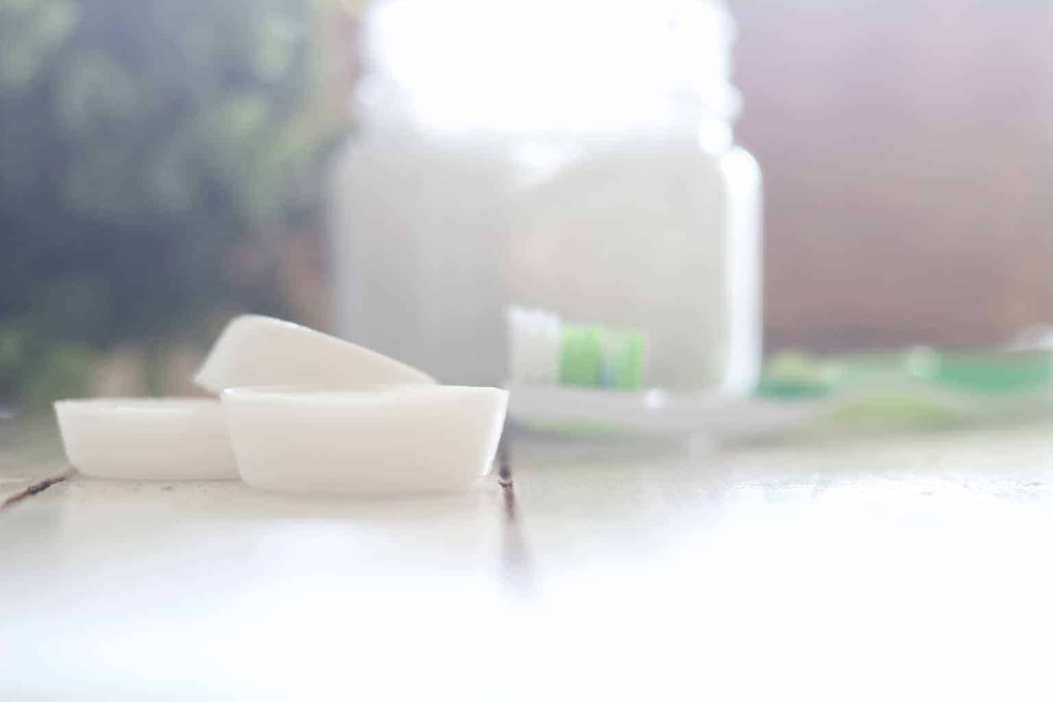 Coconut oil pods on table with toothbrush and mason jar.