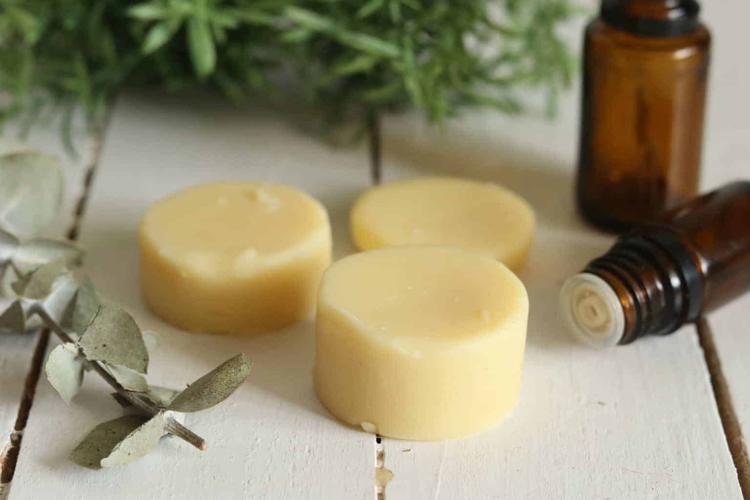 All-natural beeswax lotion bars with essential oils on white wood table.