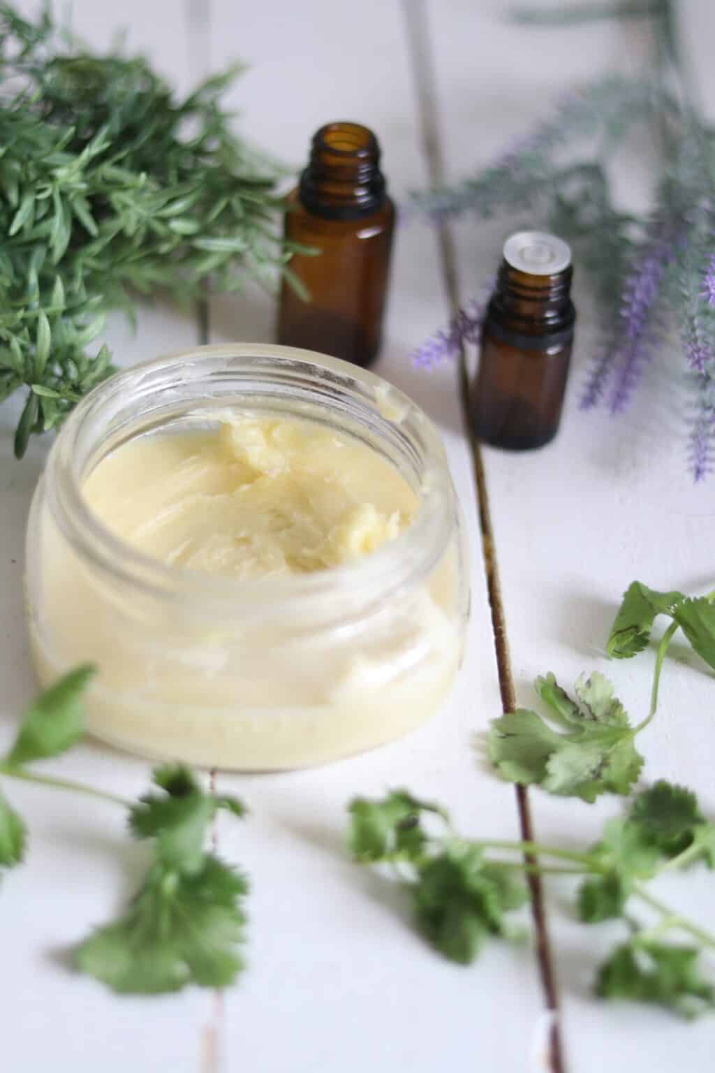Homemade whipped body butter with lavender sprigs and essential oil bottles.