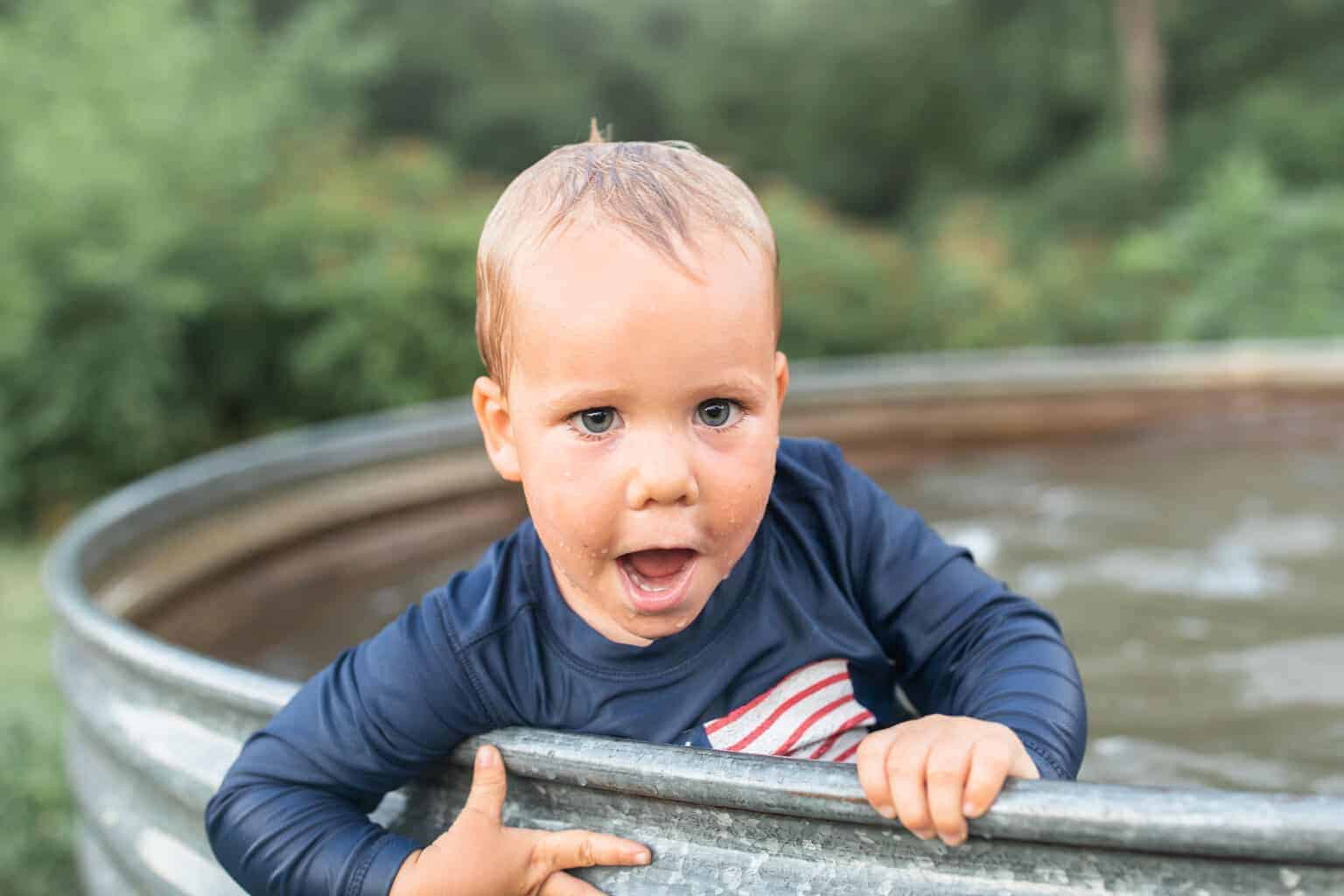 Little boy wearing long sleeve swimming shirt in a backyard tank pool.