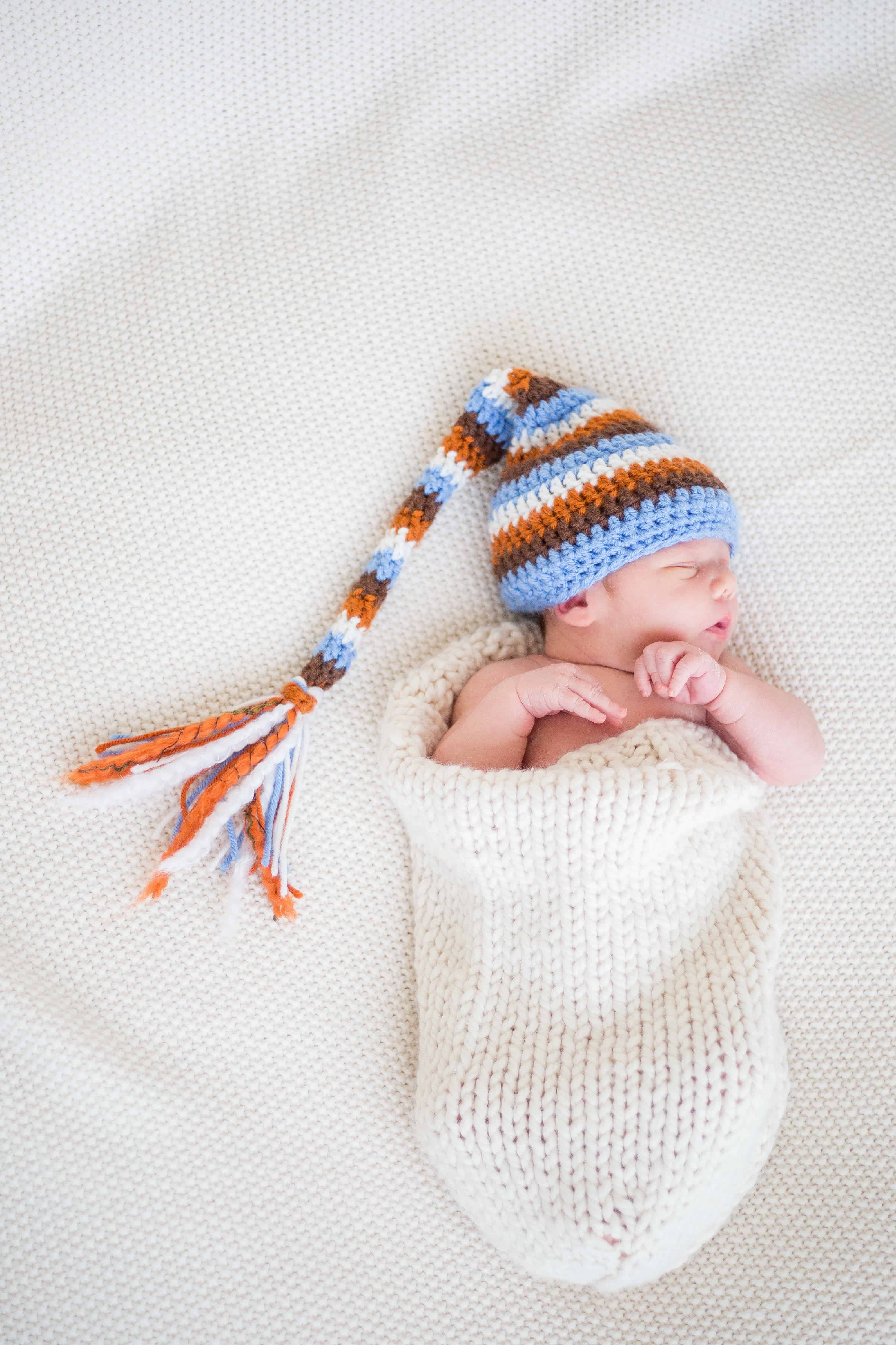 Newborn baby with stocking cap laying on white blanket.