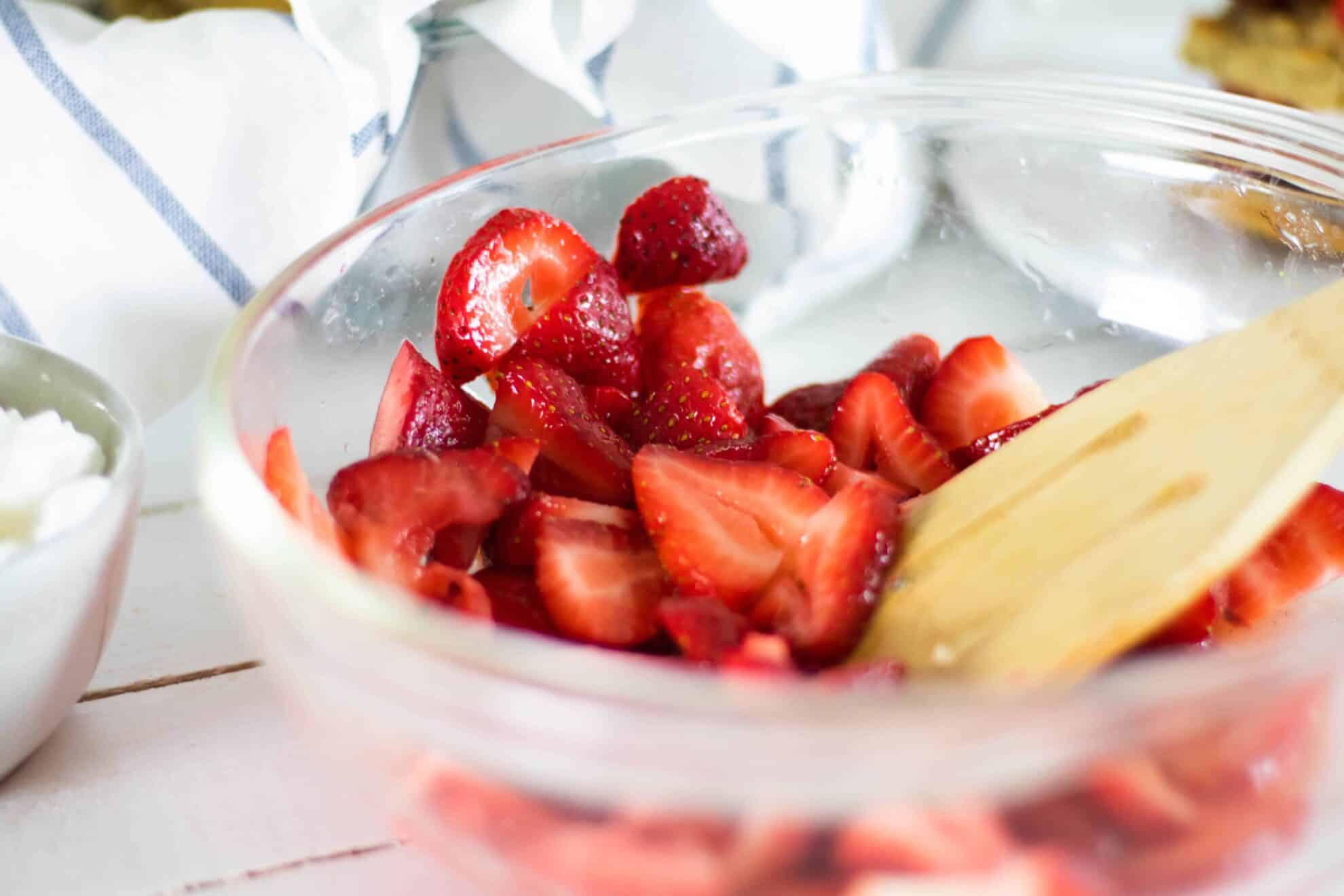 Sliced strawberries in glass bowl on wooden table.