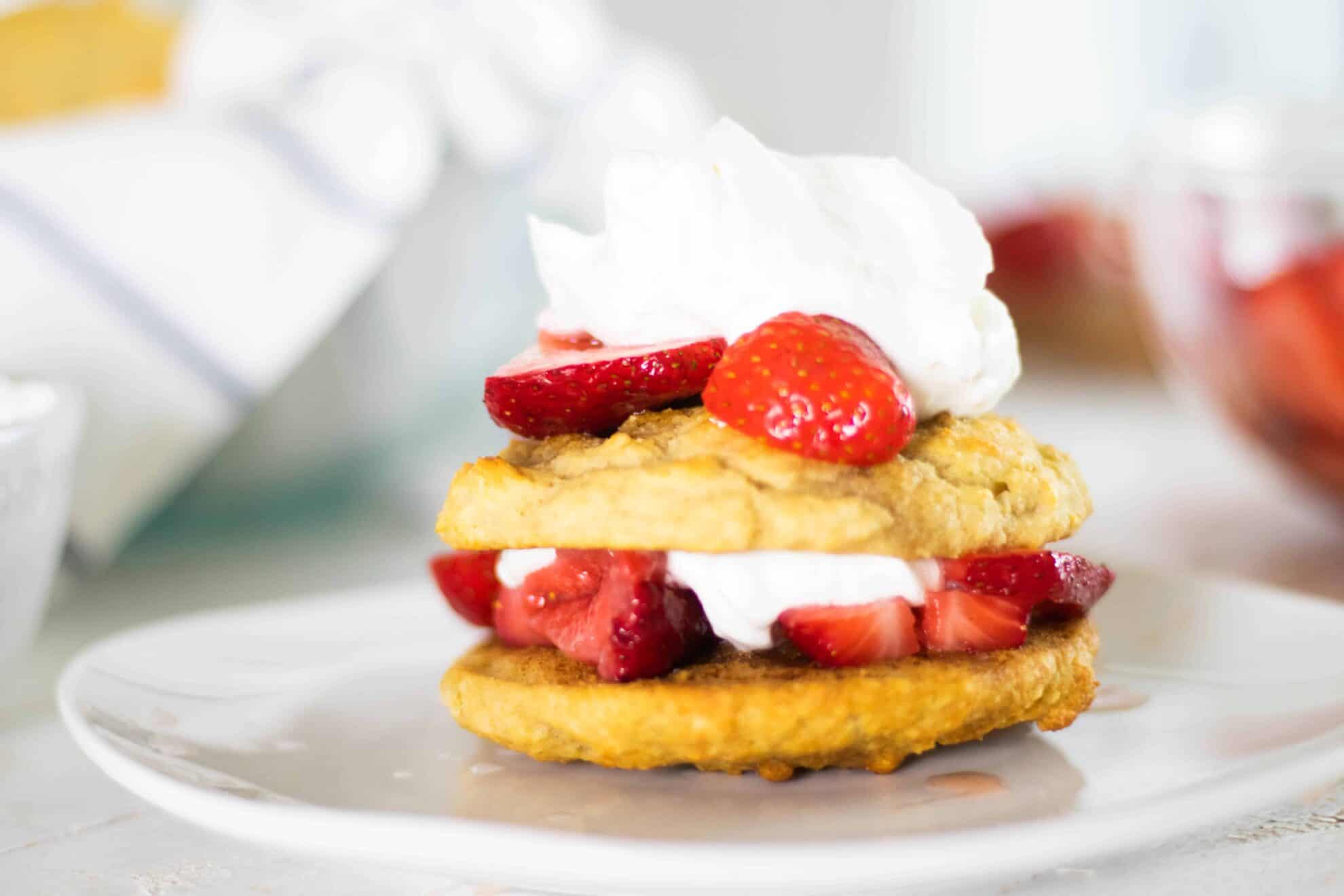 Healthy strawberry shortcake on white plate with sliced strawberries and whipped cream.