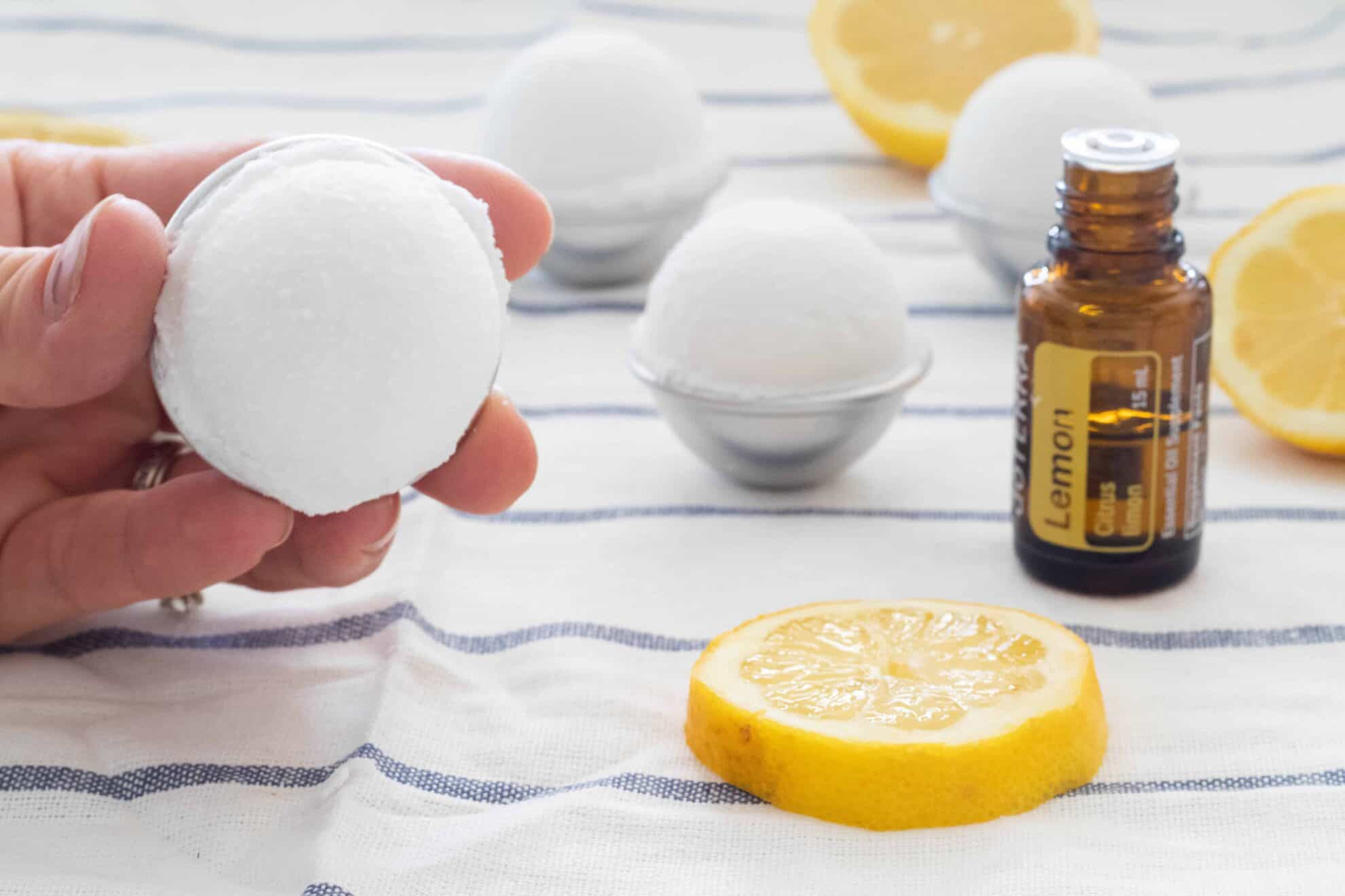 DIY toilet cleaning bombs on stripped towel with essential oil bottle and lemon slices. 