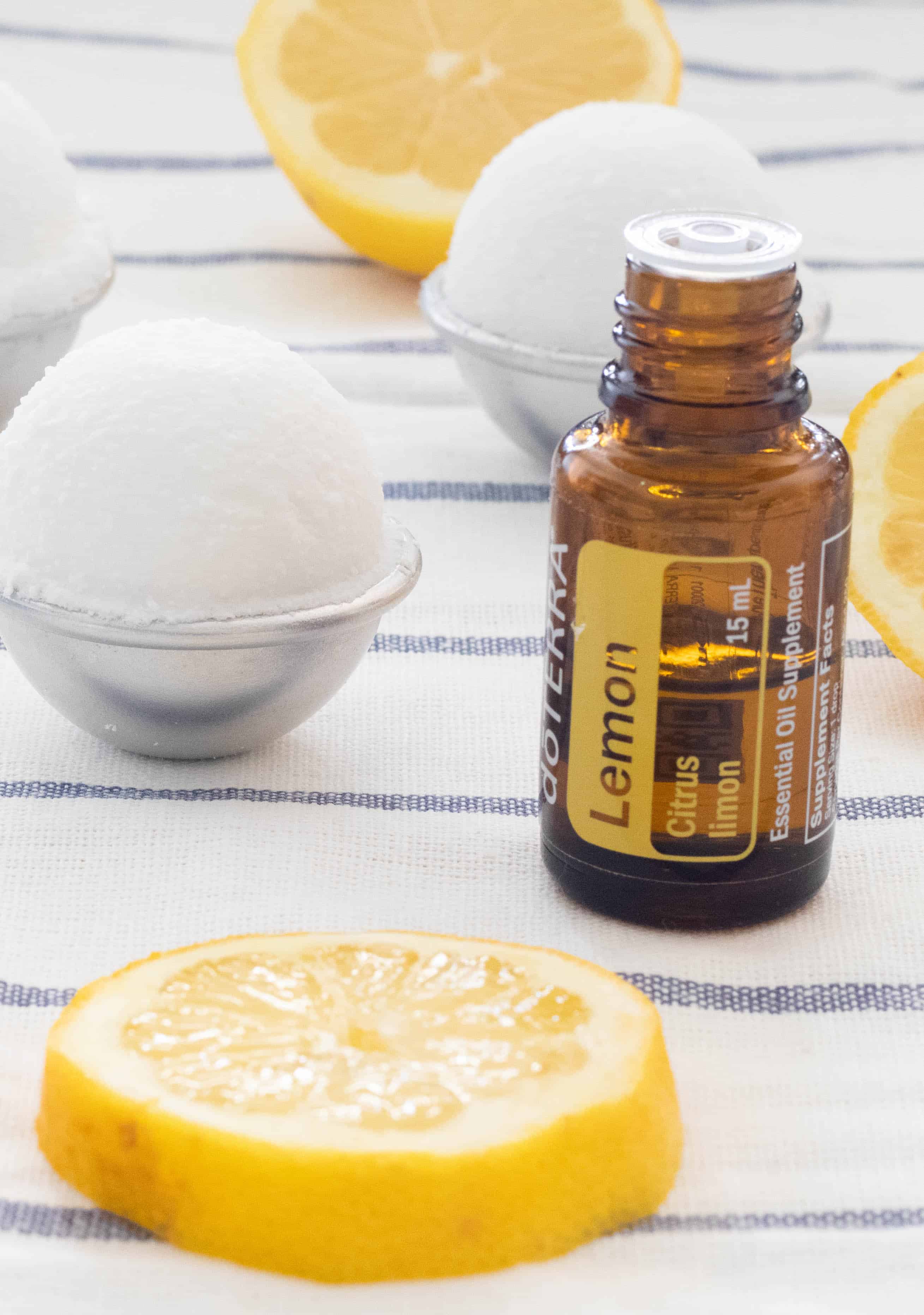 doTERRA lemon essential oil bottle, lemon slices, homemade toilet cleaning bombs on white and blue stripes towel.