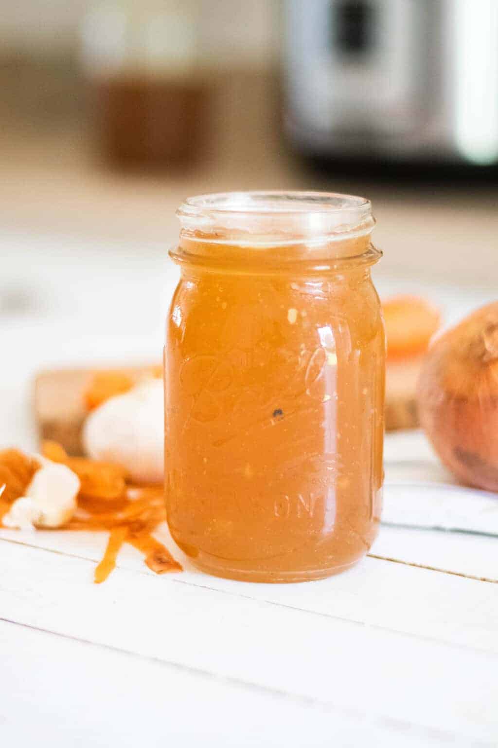 Homemade bone broth in mason jar with carrots and onions on table.