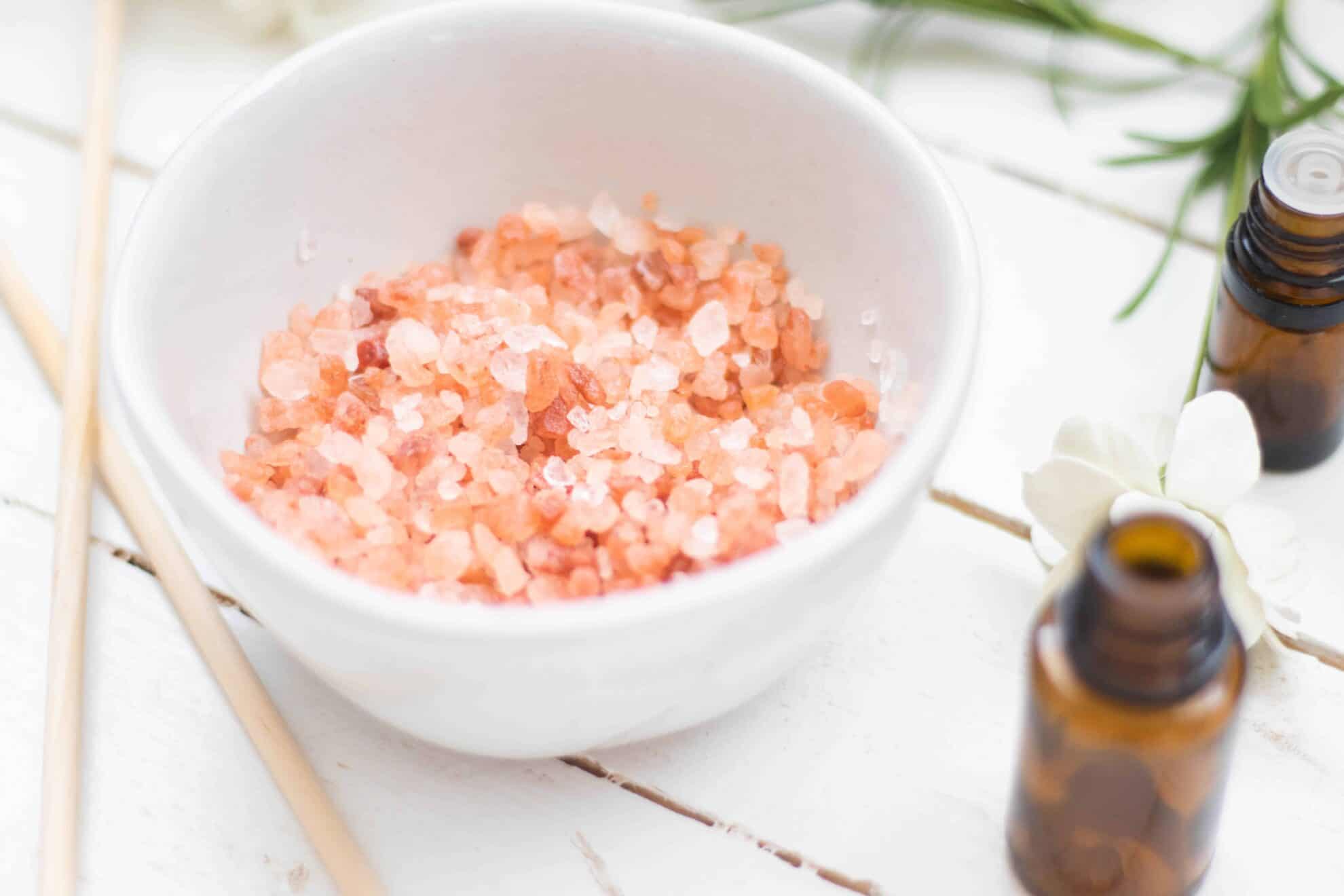 Pink salt in glass bowl on white table with essential oil bottles.