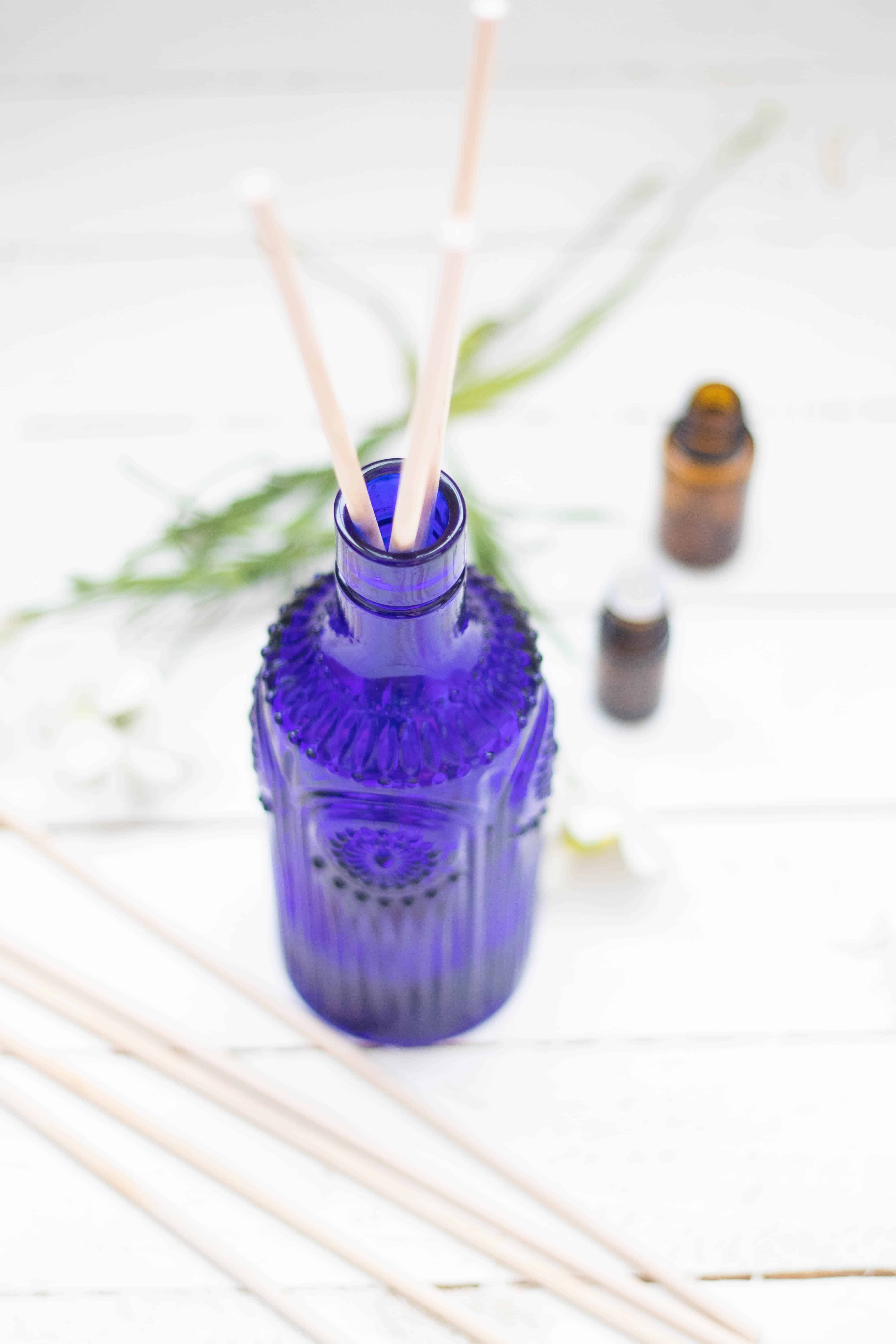 Essential oil reed diffuser on white wooden table with amber colored essential oil bottles.