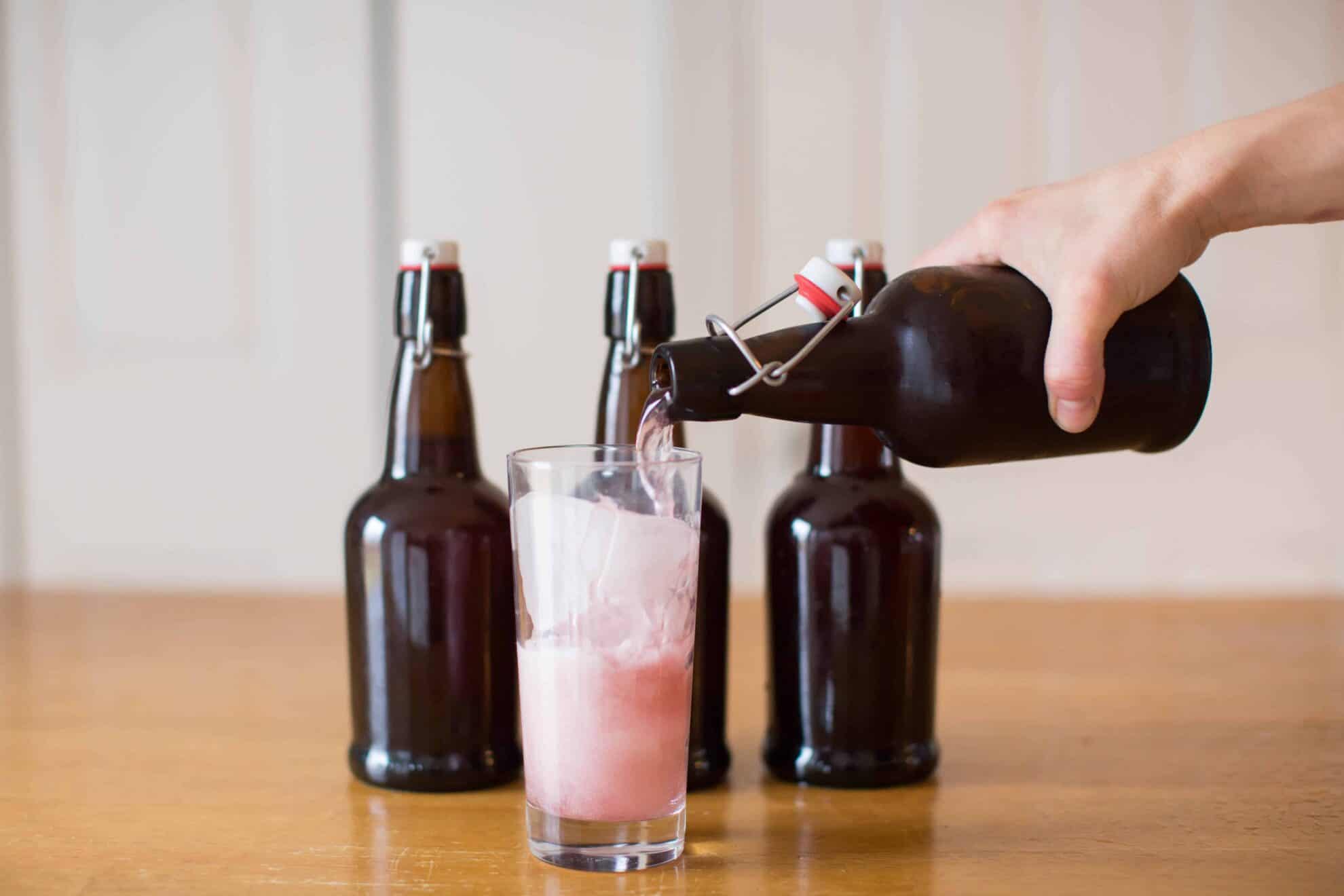 Pouring grape soda into glass of ice on table.