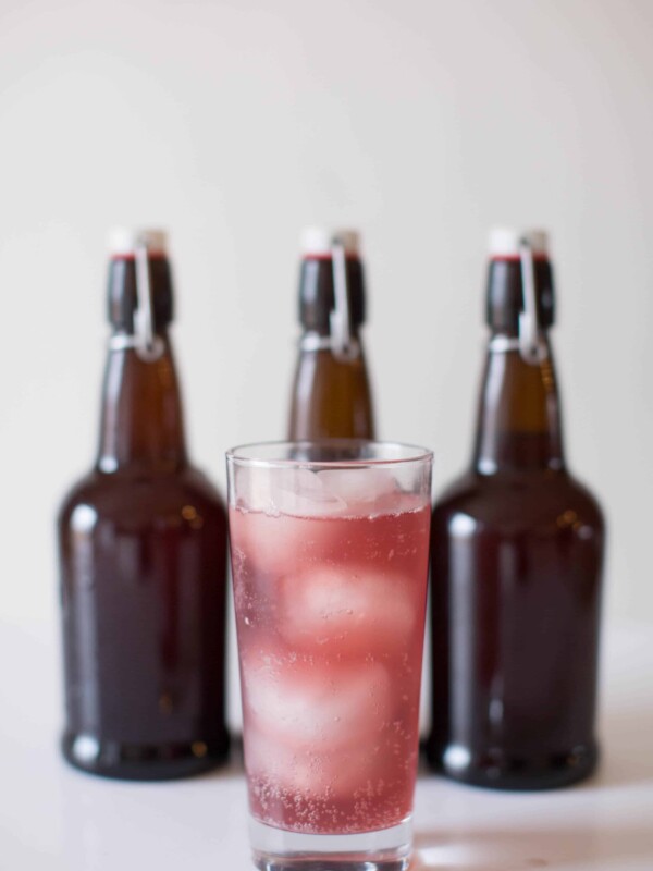 Grape water kefir in glass with brown flip top soda bottles in back.