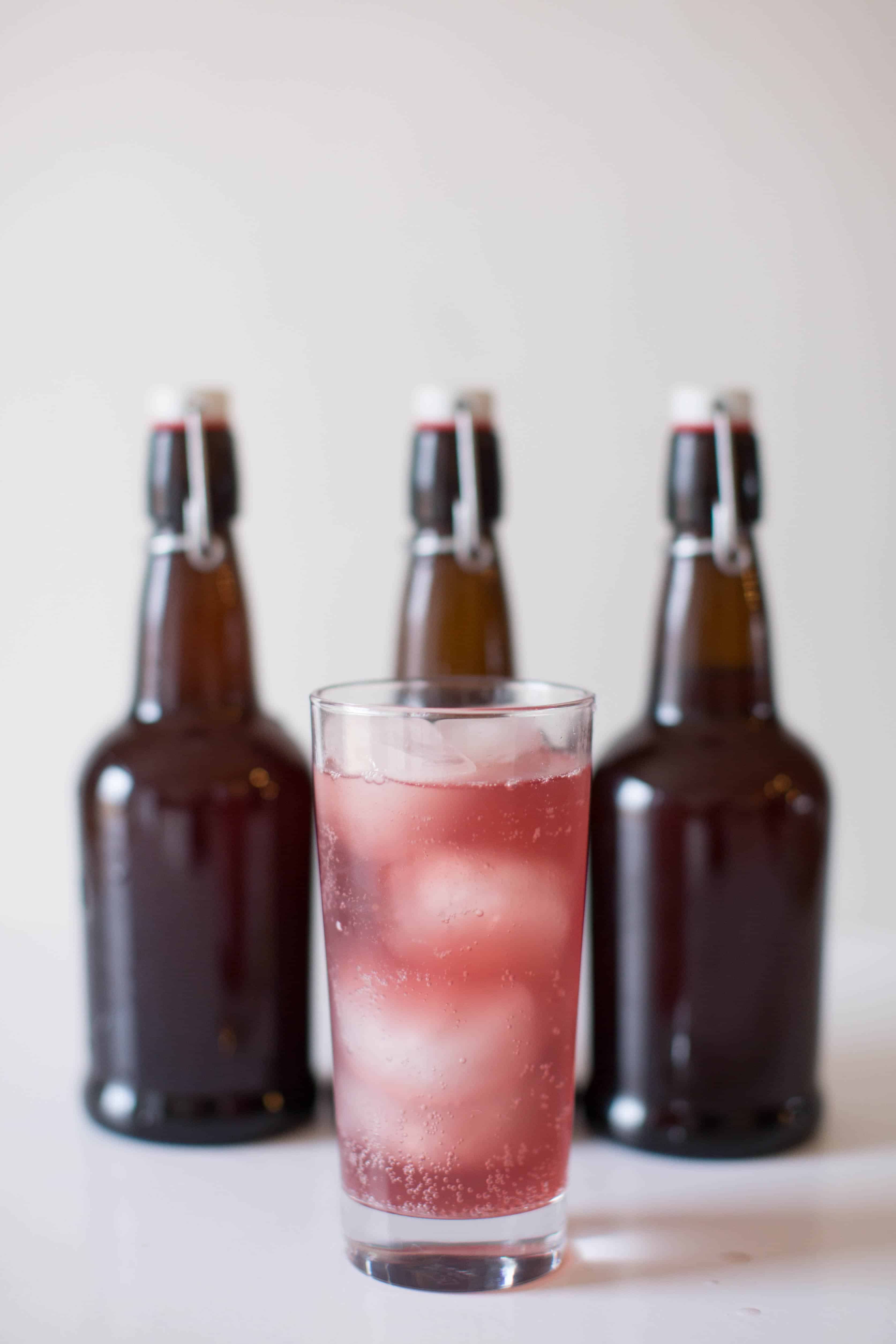 Grape water kefir in glass cup with amber flip top soda bottles in background.