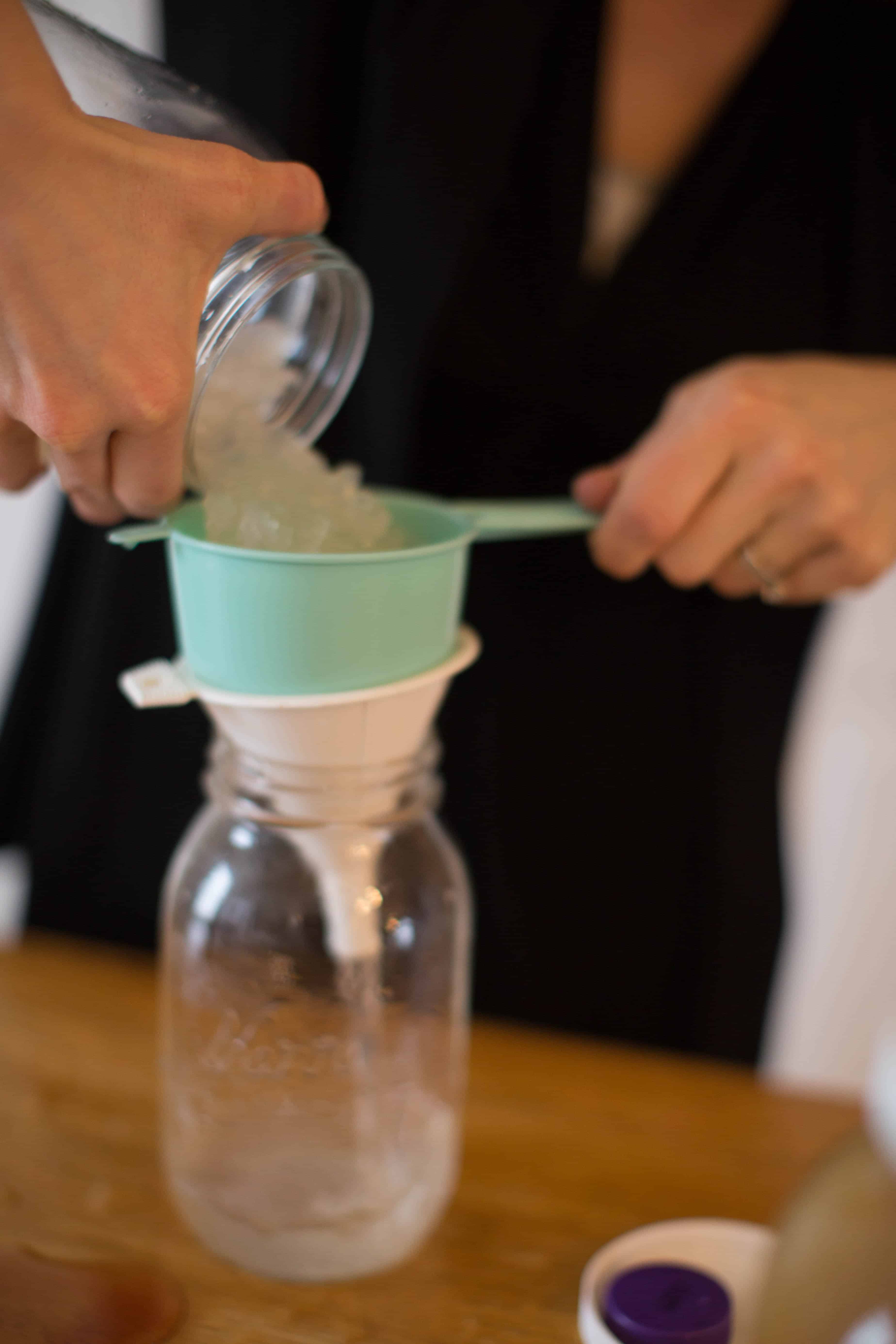 Straining water kefir grains into glass mason jar.