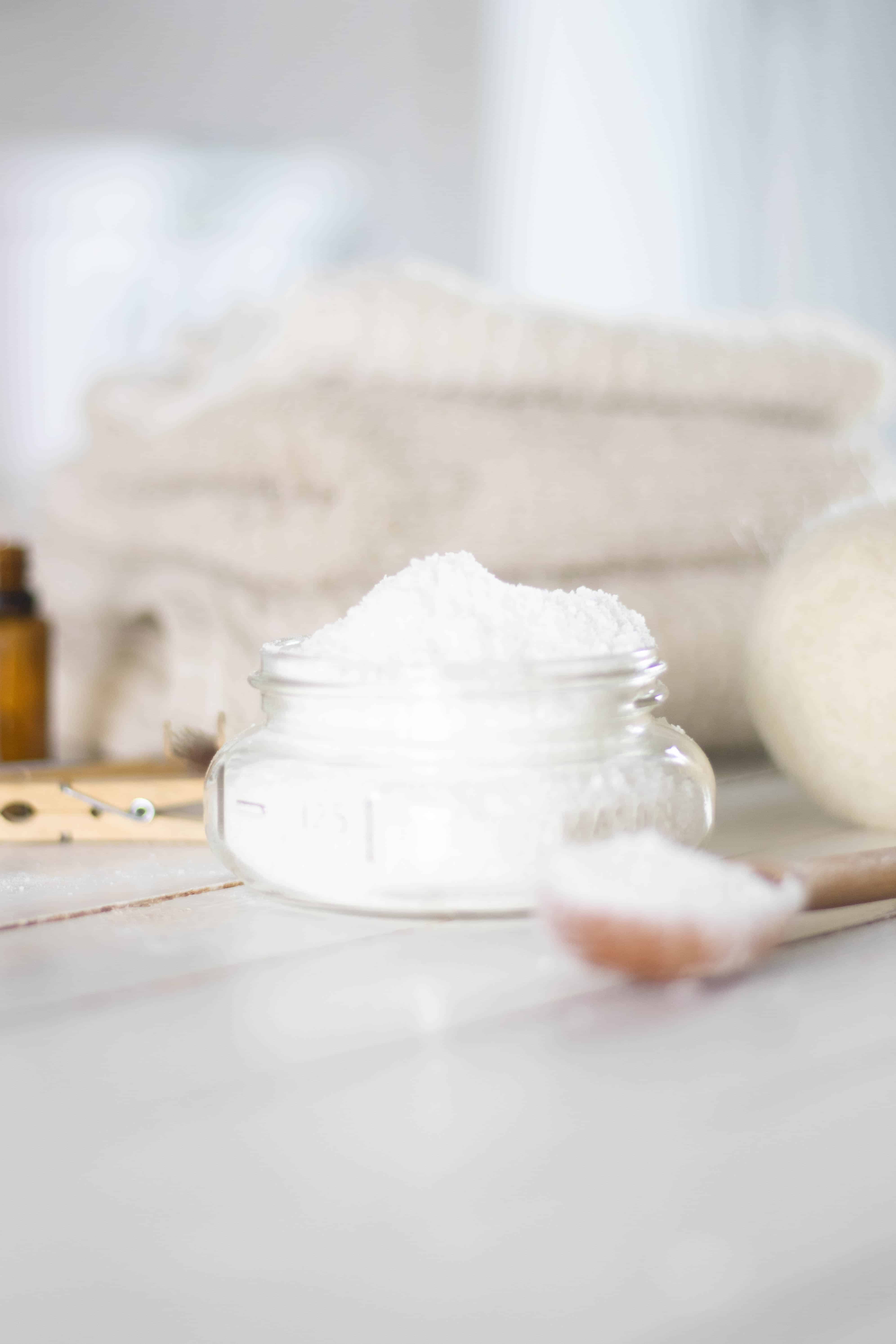 Powder laundry scent booster on white ship lap with towels, dryer ball and clothes pin in background.