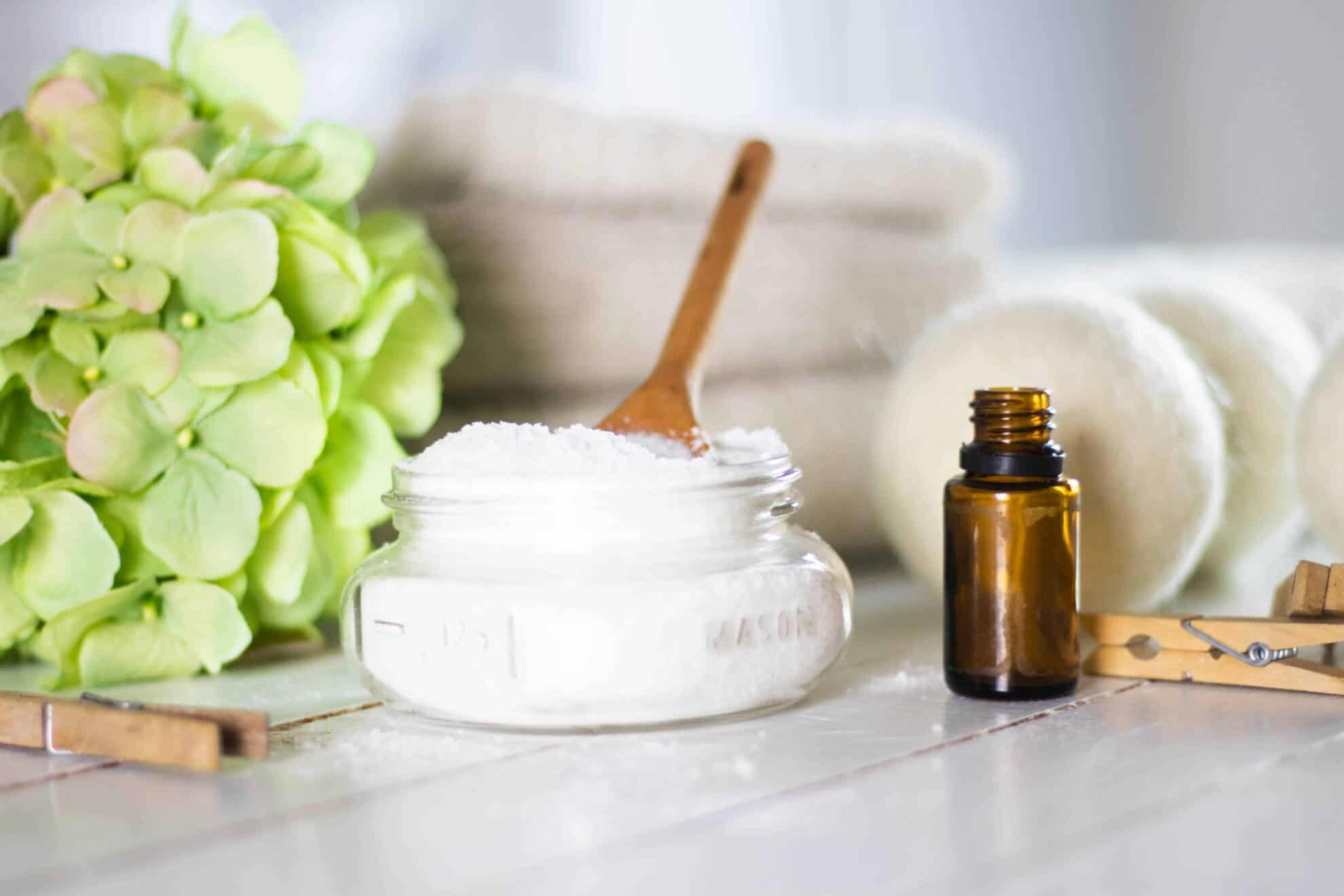 Epsom Salt and baking soda mixture in mason jar on white shiplap with dryer balls and amber colored essential oil bottle.